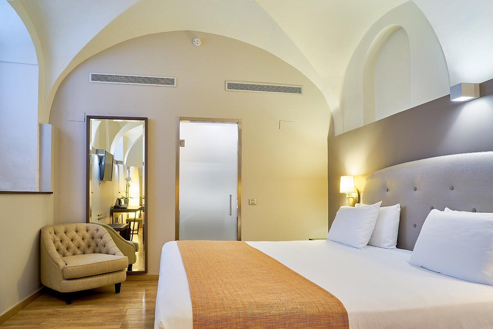 Een hotelkamer met een groot bed, een stoel, een bureau met een lamp en een deur.