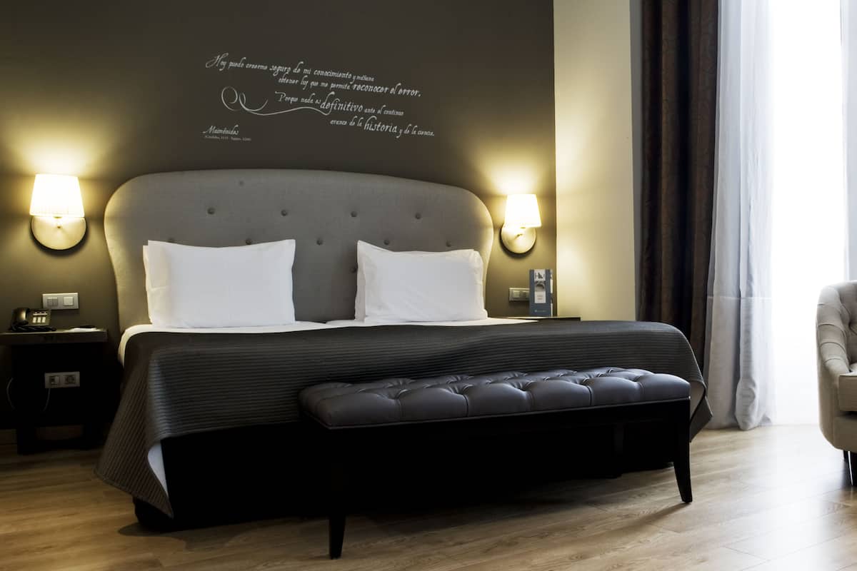 Un dormitorio moderno con una cama grande, dos lámparas de noche y una cita en la pared.