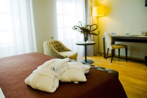 A hotel room with a bed, two chairs, a small round table with a lamp, and a vase with plants.