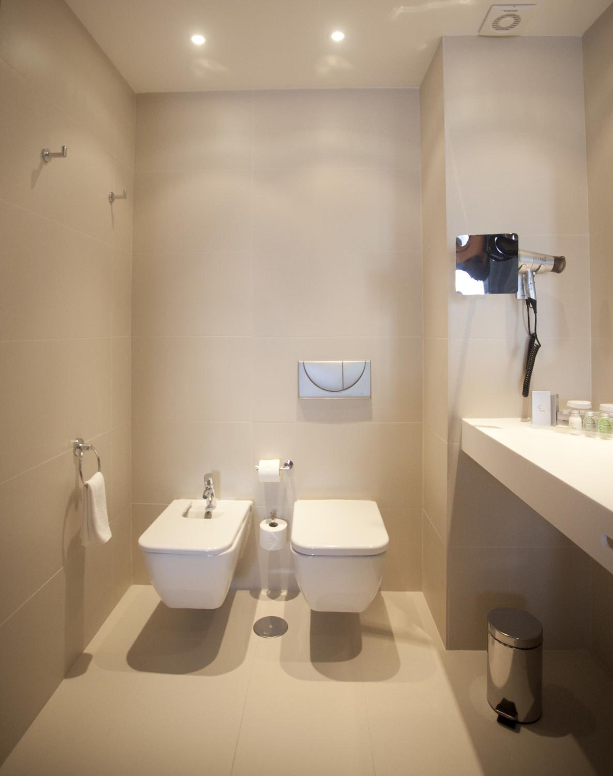 Un baño moderno con bidé, inodoro, lavabo y un cesto de basura.