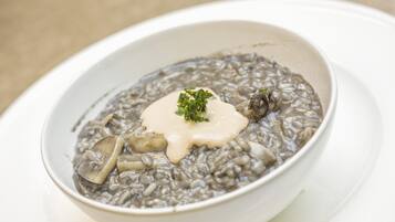 Un plato de risotto negro con setas y una cucharada de crema, decorado con perejil.