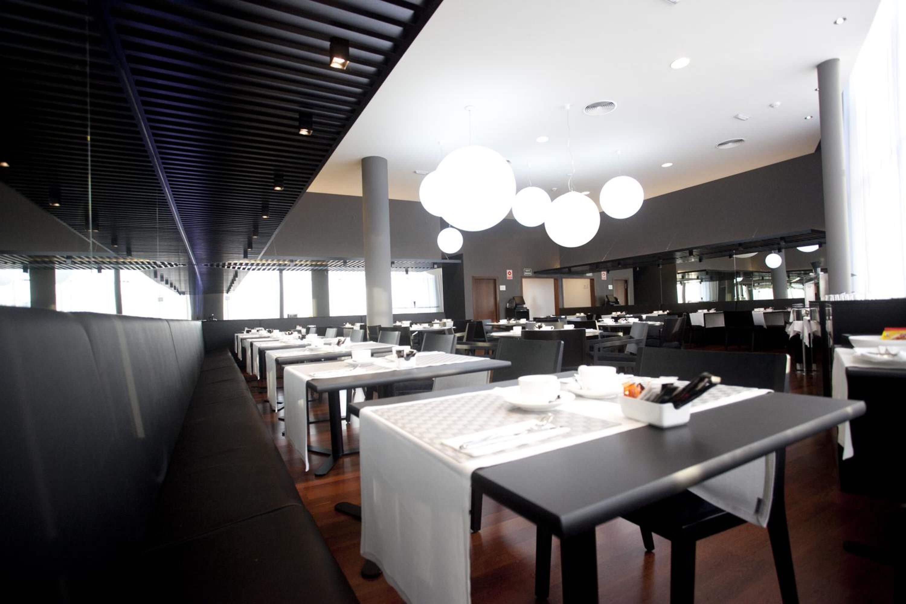 Een modern restaurant met lange gedeelde tafels, hoge plafonds en hanglampen.