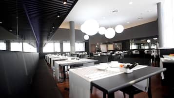 Een modern restaurant met lange gedeelde tafels, hoge plafonds en hanglampen.