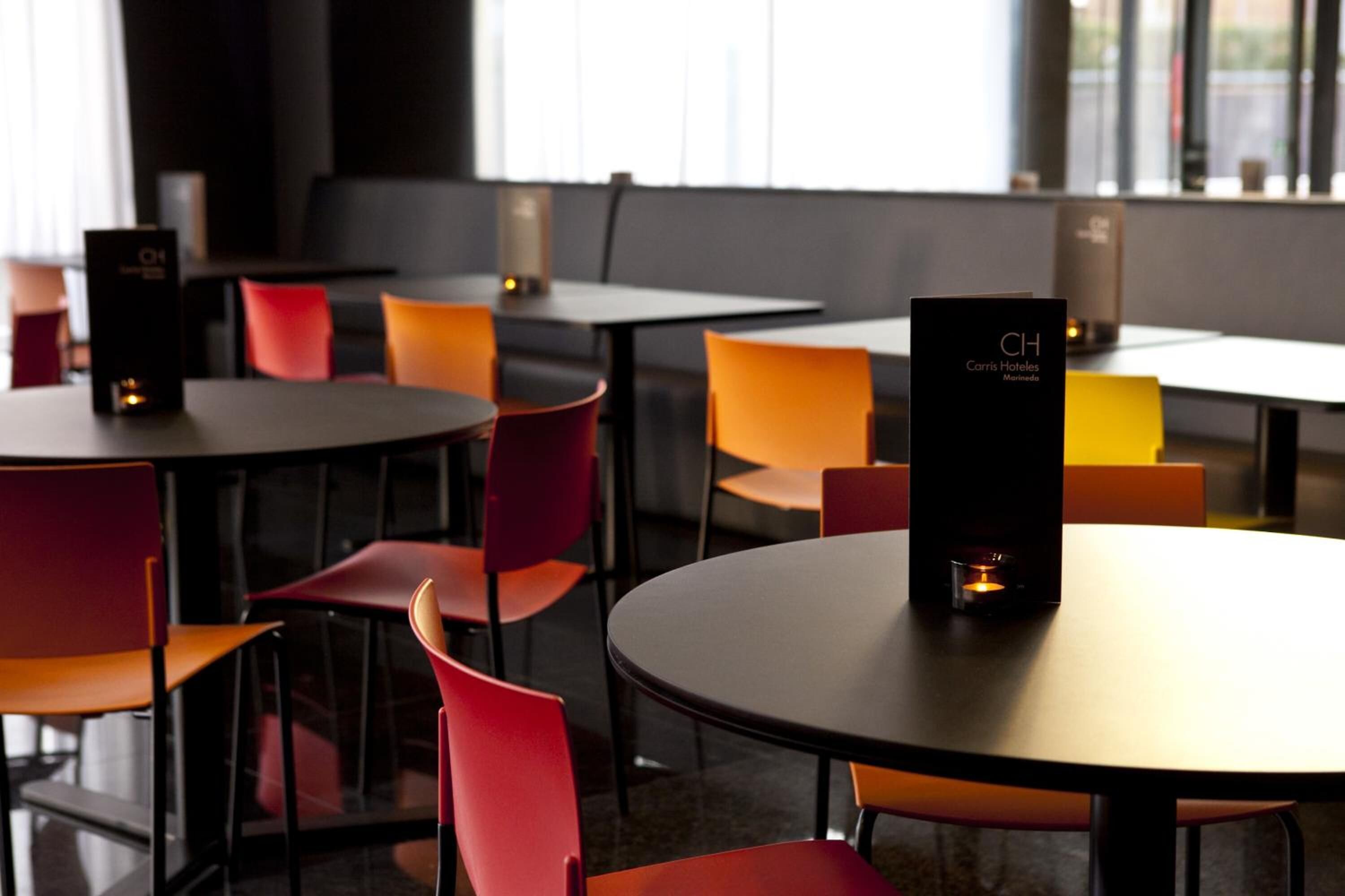 A modern hotel lobby with round tables and vibrant orange chairs.