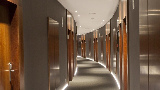 Un pasillo largo en un hotel moderno, con puertas de madera y piso alfombrado.
