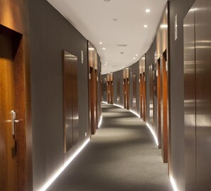 Un pasillo largo en un hotel moderno, con puertas de madera y piso alfombrado.