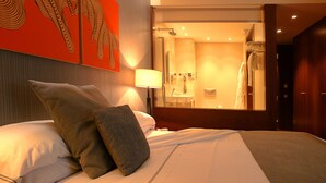 Una habitación de hotel con una cama, almohadas, una mesita de noche, una lámpara y un espejo grande.