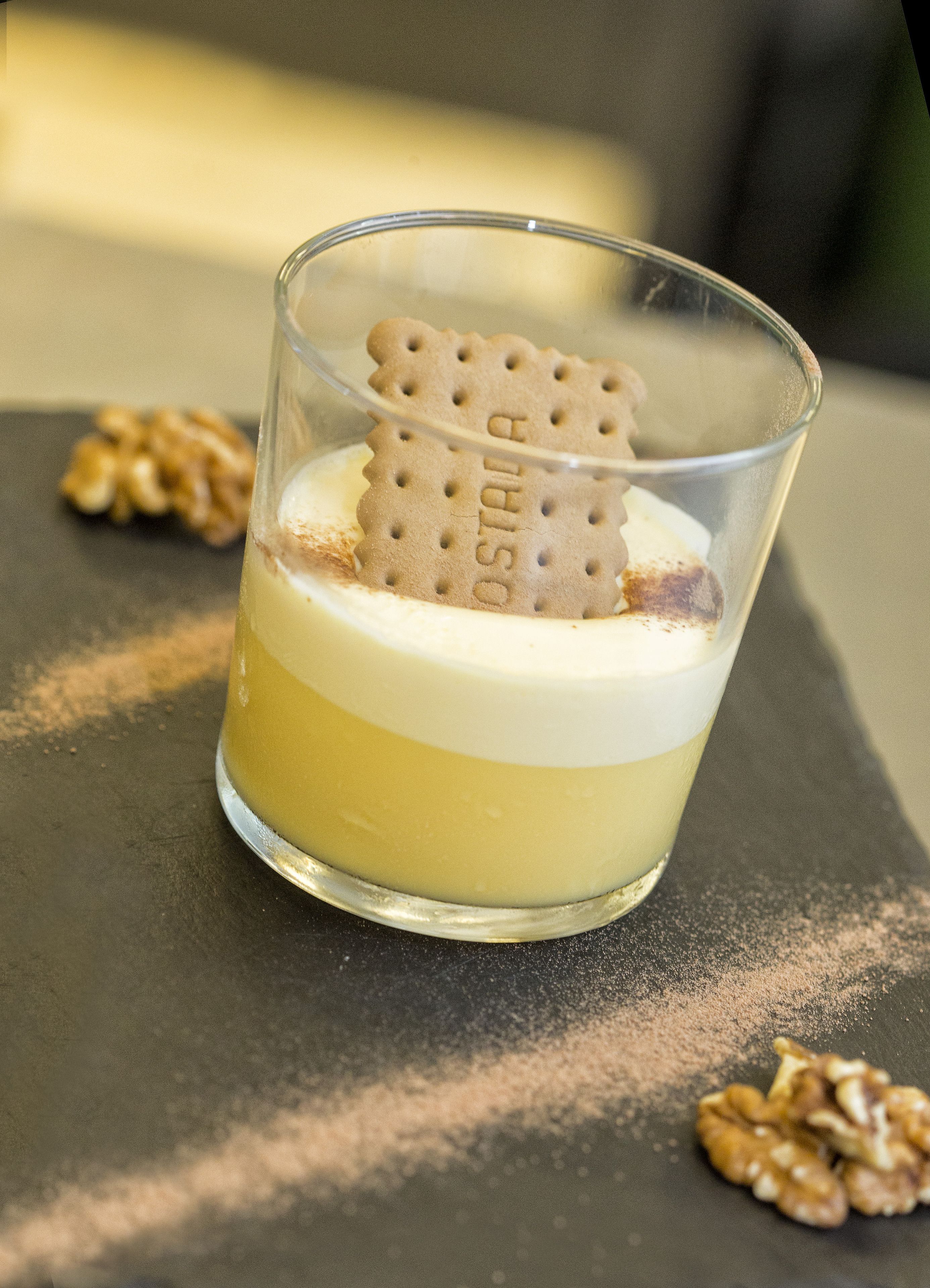 Un postre en un vaso, con una galleta de obleas encima, sobre una superficie oscura con nueces esparcidas.