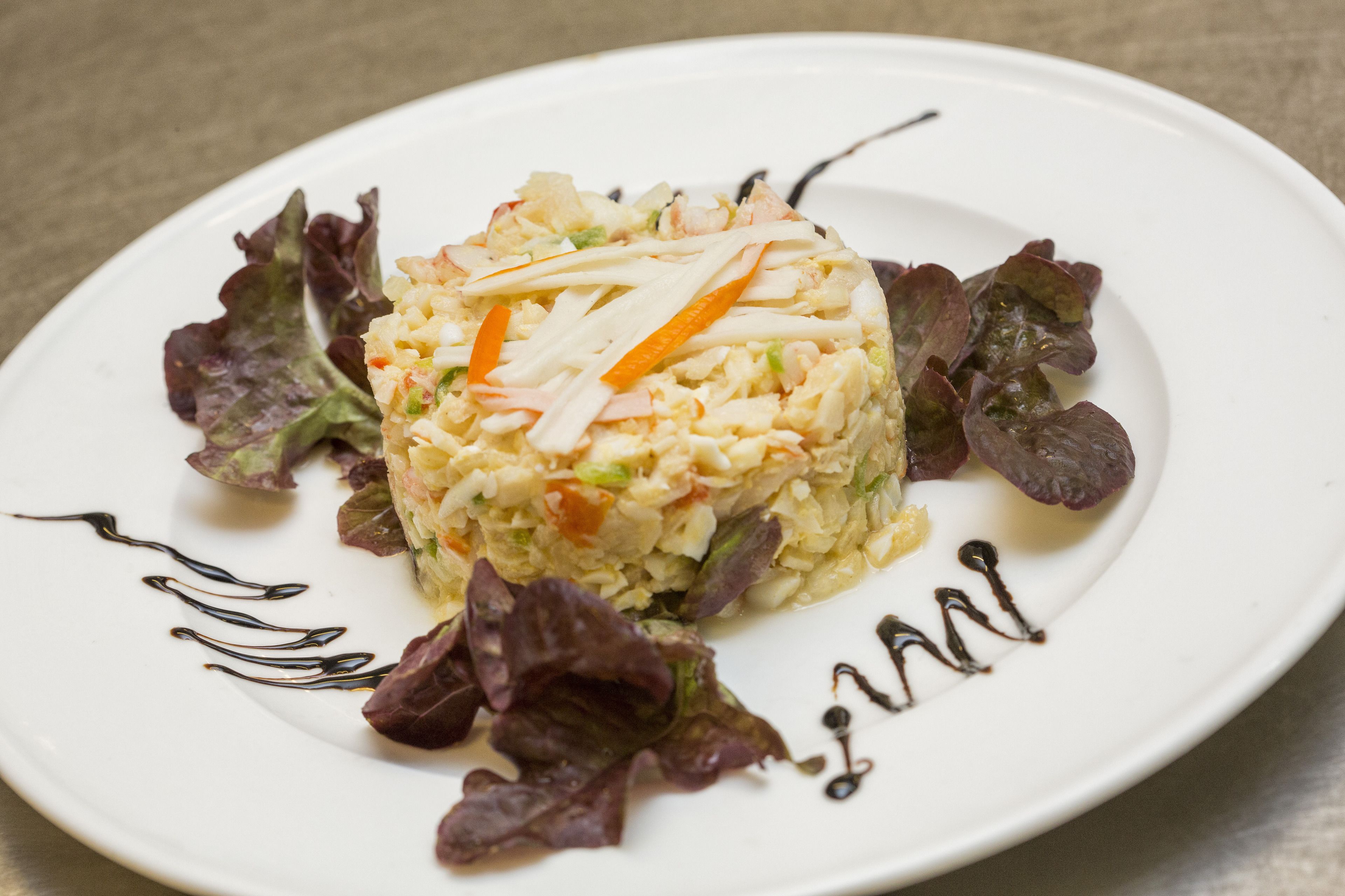 Un plato blanco con una ensalada en capas y algunas hojas verdes.
