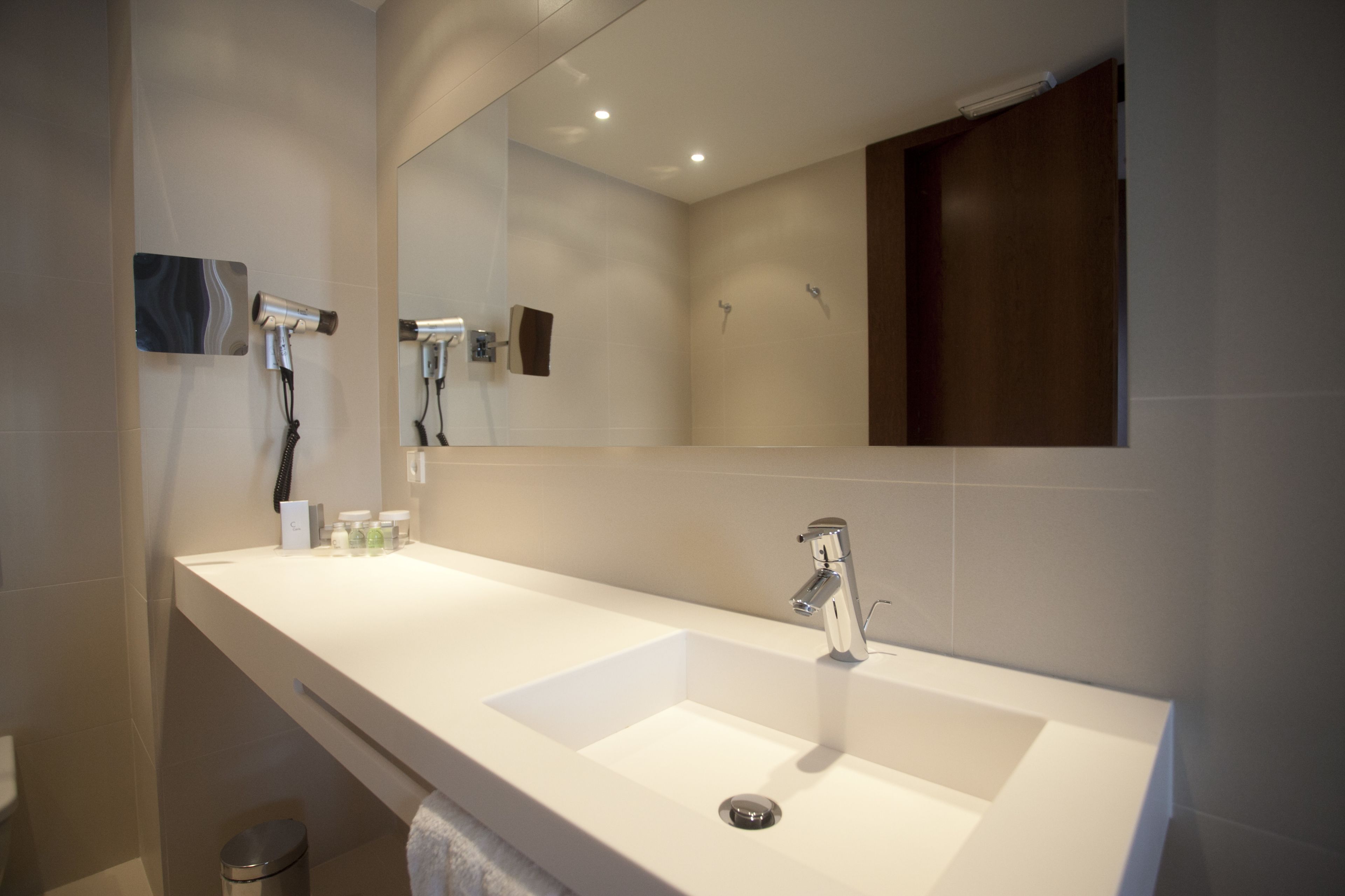 A modern bathroom with a large white sink, a mirror, and a hairdryer mounted on the wall.