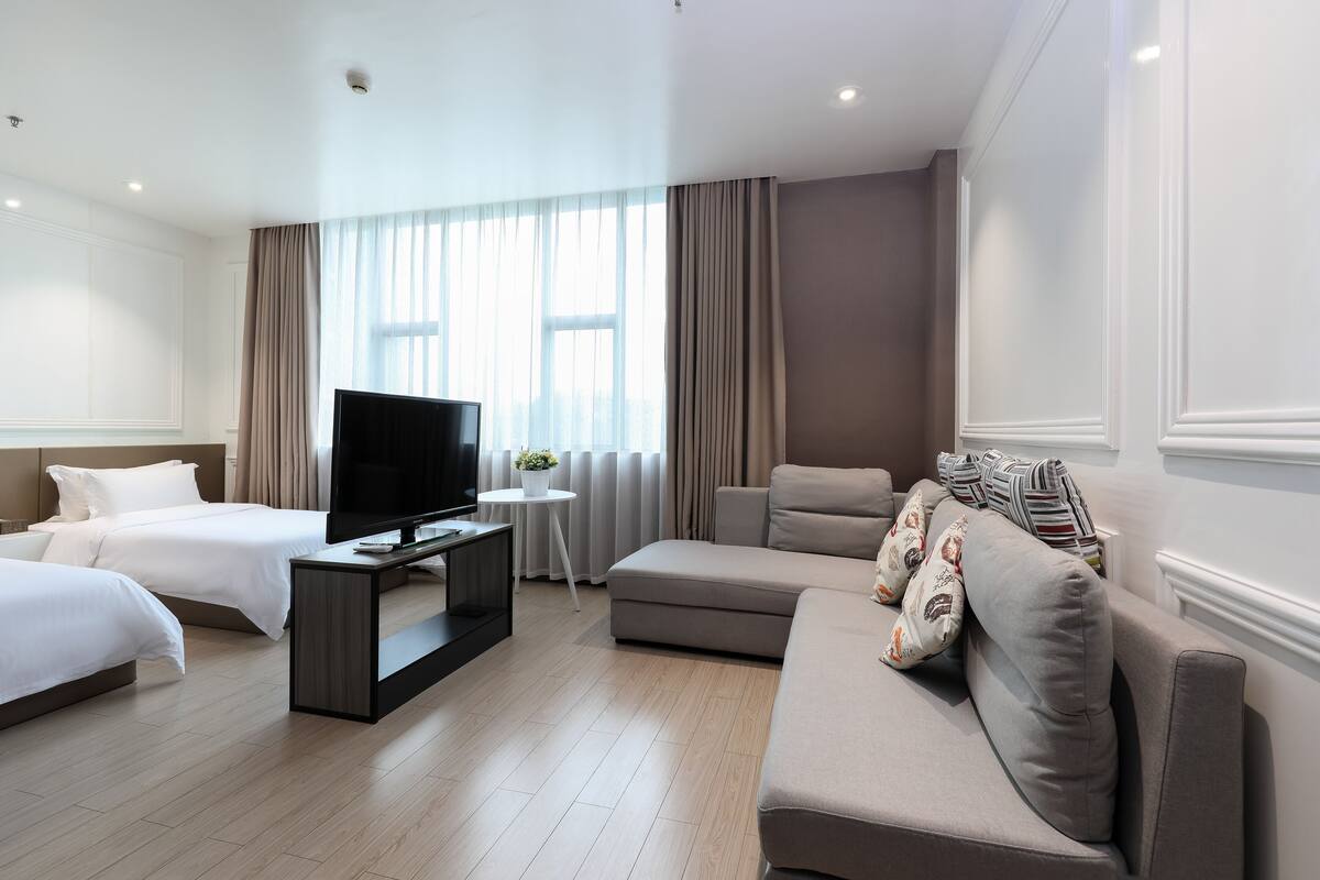 Une chambre d’hôtel moderne avec un grand lit, un canapé, une télévision et une petite table agrémentée d’une plante.