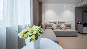 A modern living room with a grey sofa, a white vase with flowers, and a wooden floor. - Hengdong Business Hotel - Guangzhou (Guangzhou)