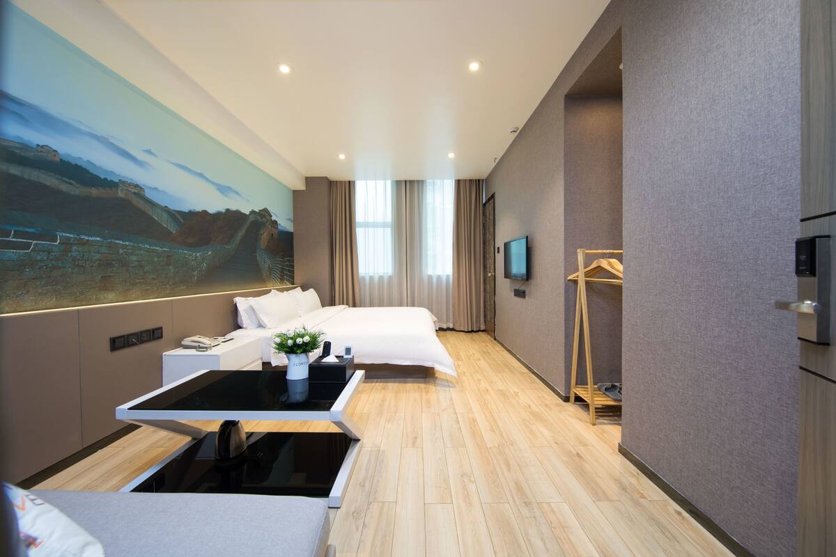 Une chambre d’hôtel moderne dotée d’un grand lit, d’un bureau avec un ordinateur, d’une télévision à écran plat et d’un tableau représentant un paysage accroché au mur.