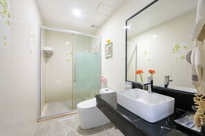 Un baño moderno con ducha envuelta en vidrio, inodoro blanco, un lavamanos grande de color blanco y encimera negra.