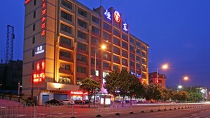 A multi-story hotel with illuminated signage, a parking area, and a street view with trees and vehicles. - Hengdong Business Hotel - Guangzhou (Guangzhou)