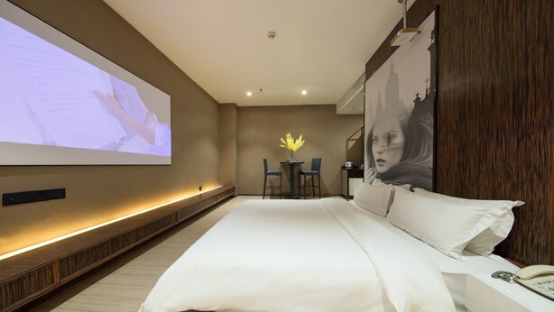 A modern hotel room with a large bed, a desk with two chairs, a small table with a vase, and a large screen on the wall. - Hengdong Business Hotel - Guangzhou (Guangzhou)