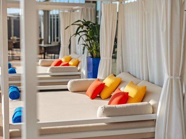 A sunlit room with a bed, pillows, a potted plant, and a window with curtains.