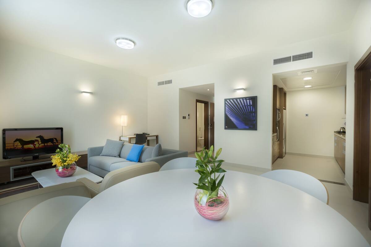 A modern living room with a round table, a sofa, a flat-screen TV, and a vase with flowers.