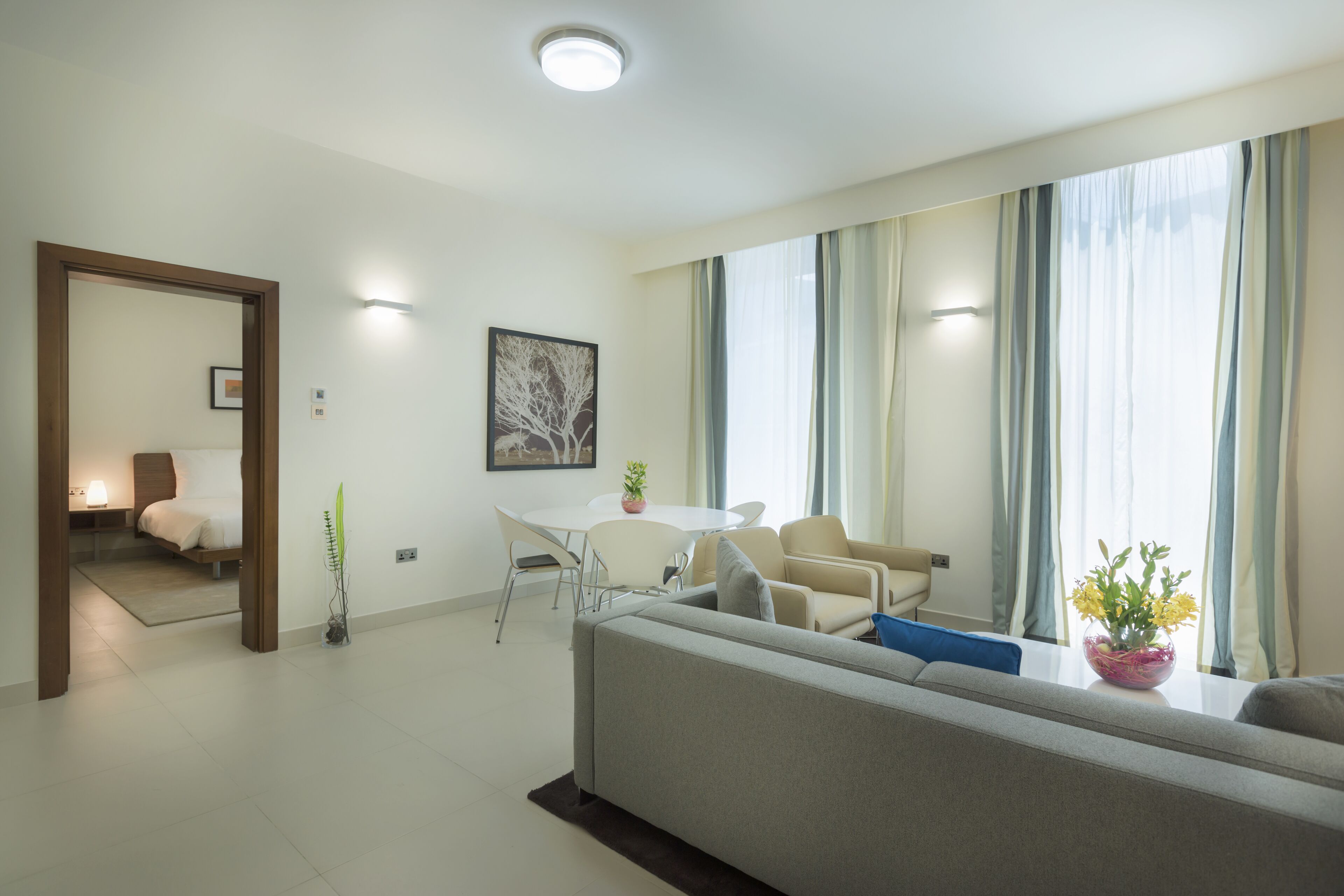 Un soggiorno moderno con un divano, un tavolo da pranzo e sedie. Si intravede un letto sullo sfondo, una pianta e un quadro appeso al muro.