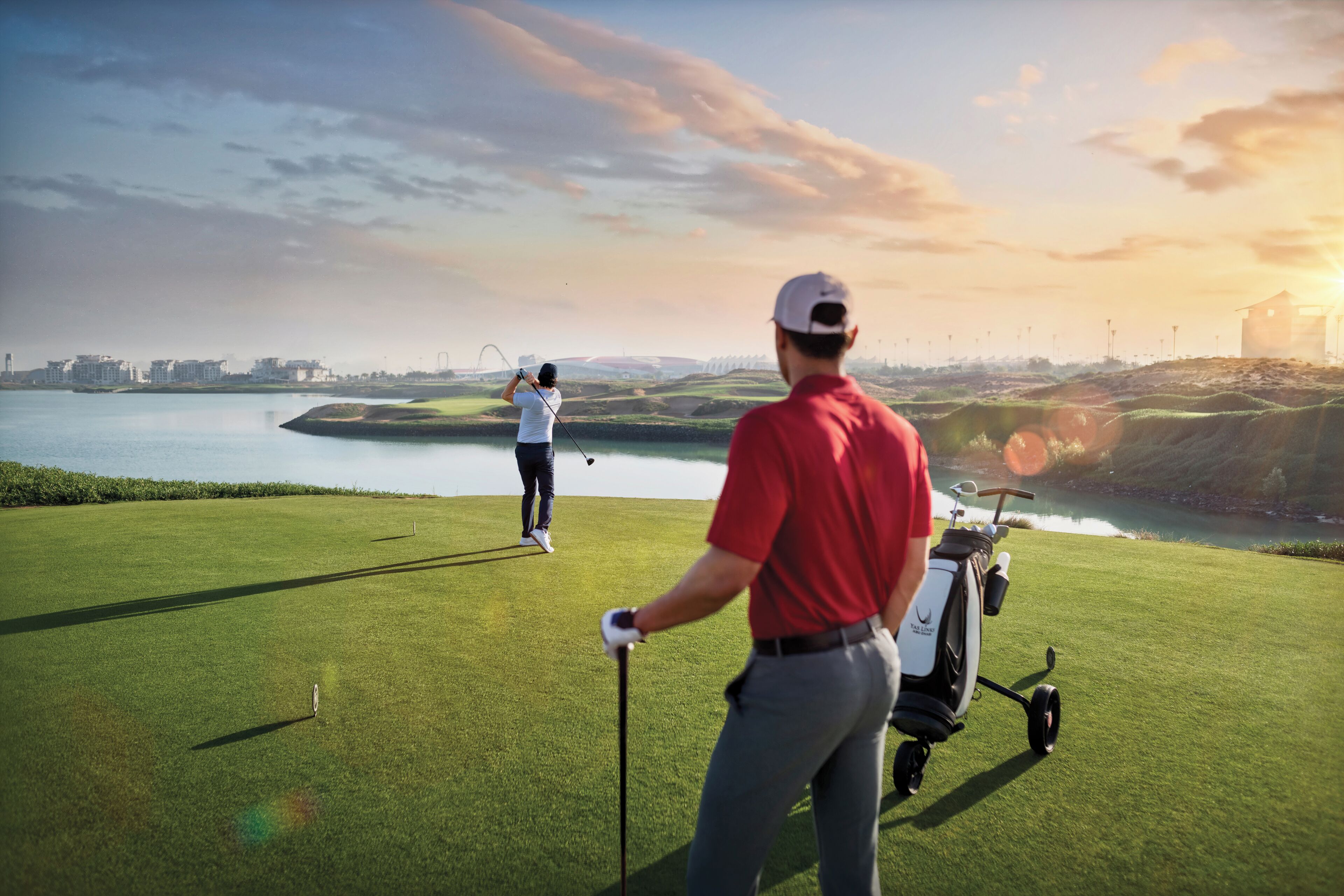 Ein Golfplatz mit einem Wasserkörper im Hintergrund, einem Golfwagen und einer Person in einem roten Hemd.