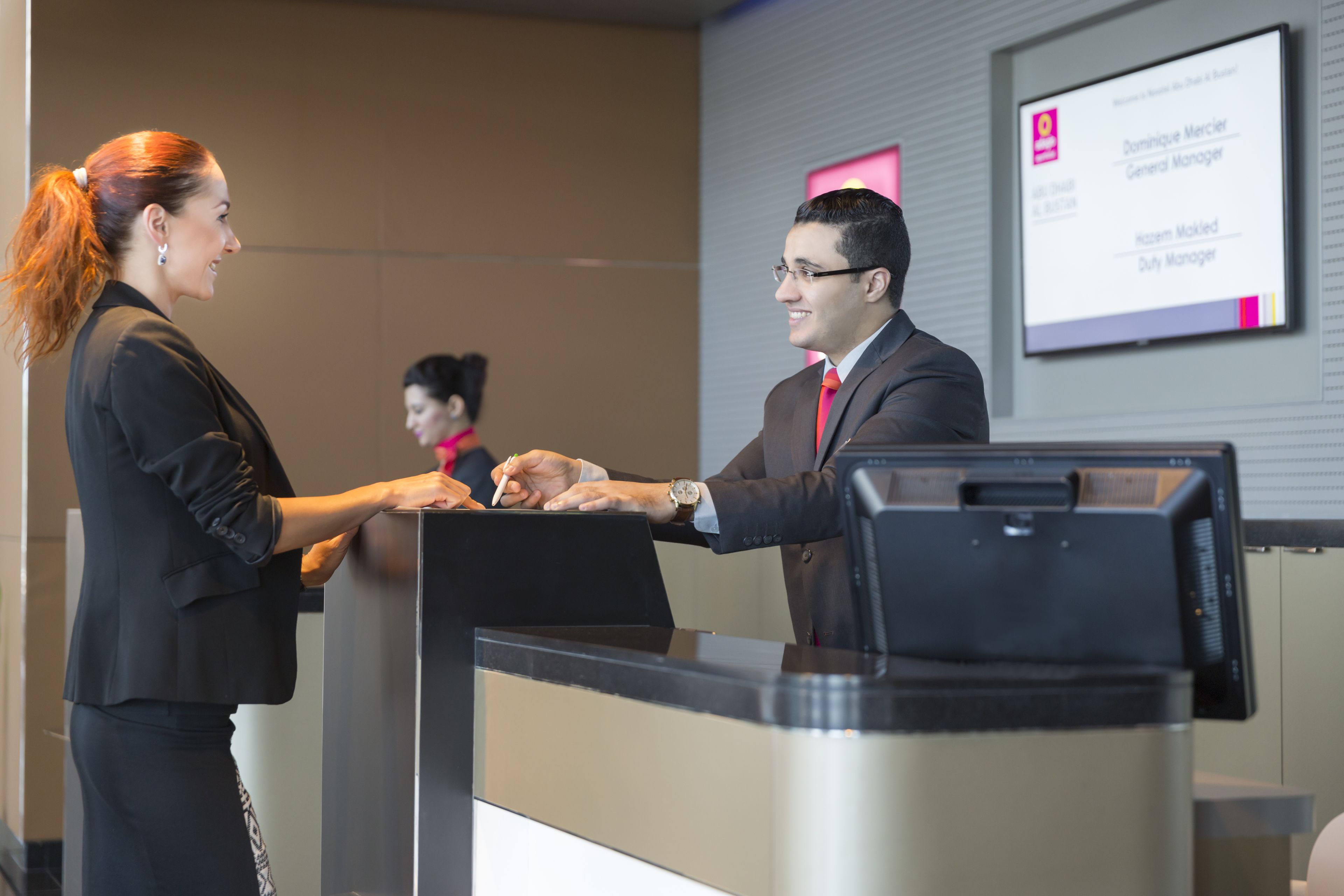 Ambiente profesional con dos personas estrechándose la mano en una recepción, una pantalla digital al fondo y un diseño de interiores moderno.