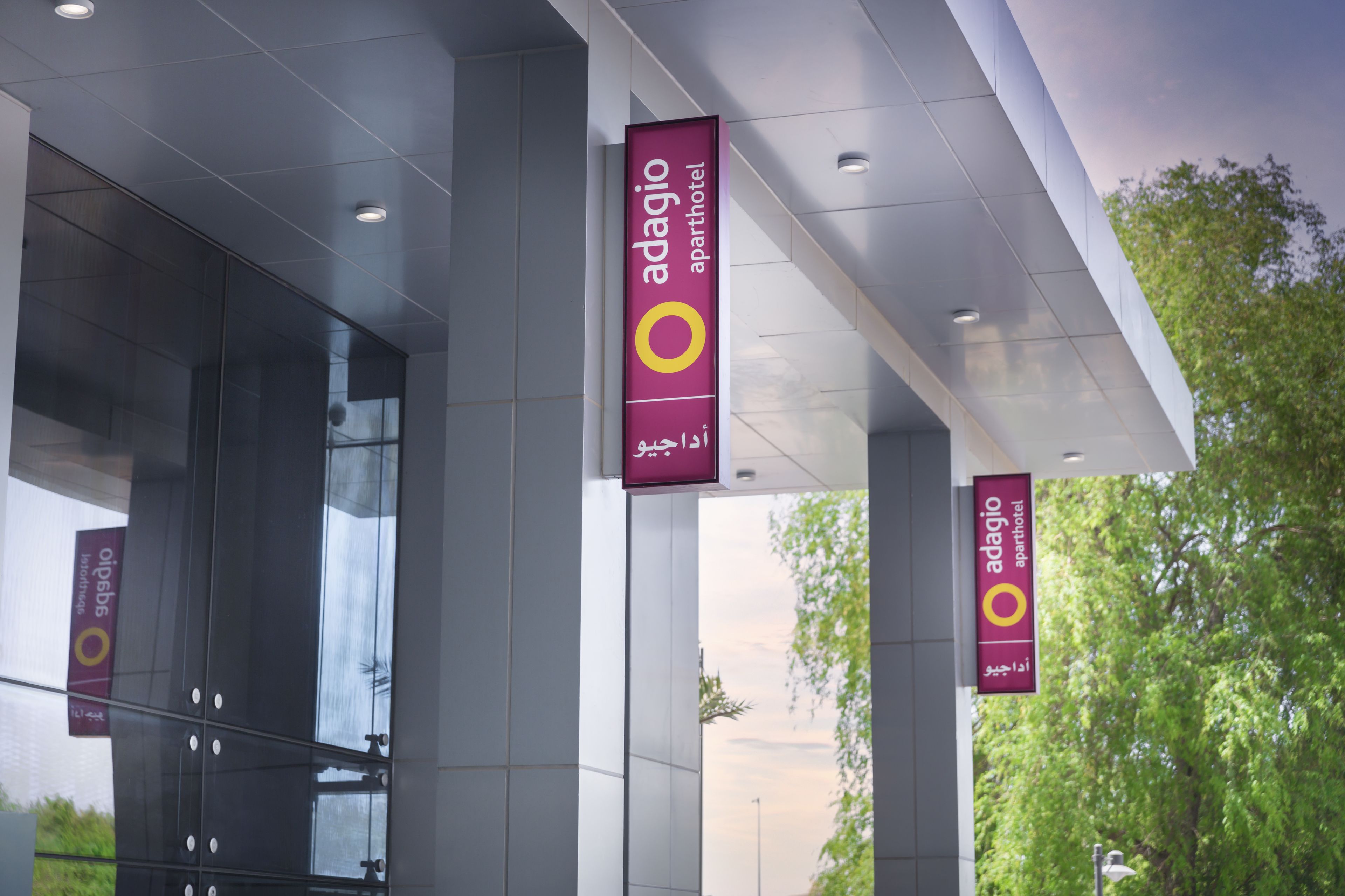 The exterior of Adagio Aparthotel with large glass windows and multiple hanging banners displaying the hotel's name.