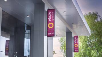 The exterior of Adagio Aparthotel with large glass windows and multiple hanging banners displaying the hotel's name.