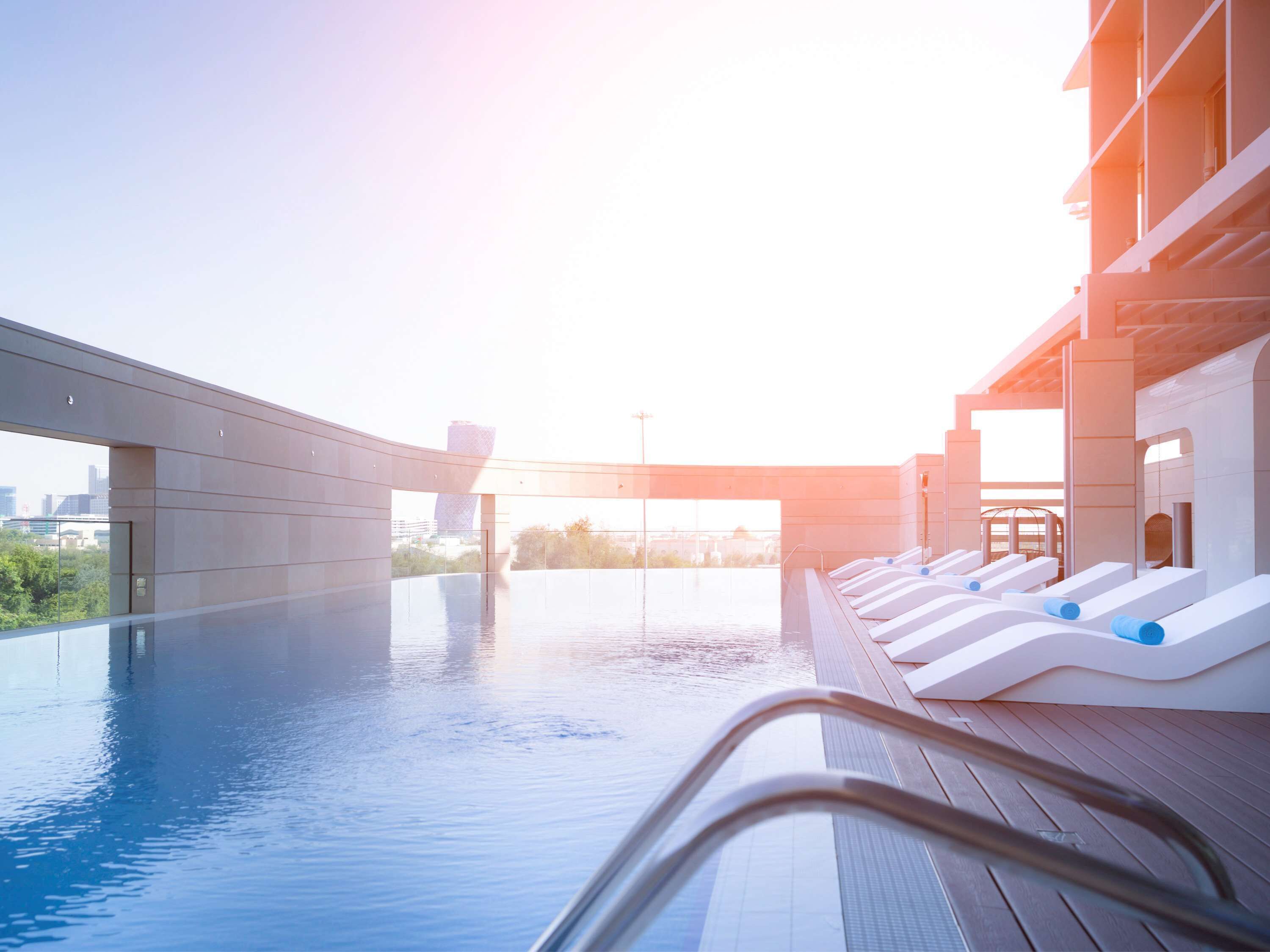 A modern outdoor swimming pool with lounge chairs and a view of the city skyline.