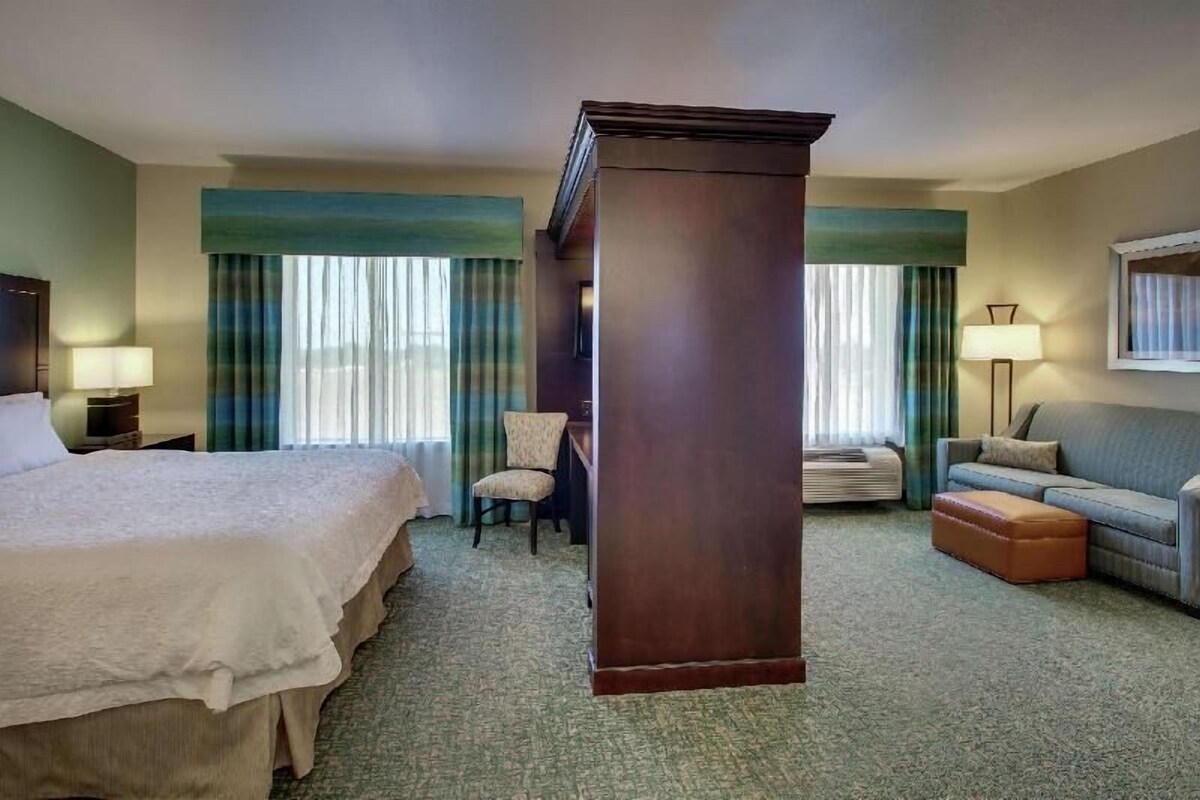 Una habitación de hotel con cama, escritorio, silla, sofá y un gran pilar.