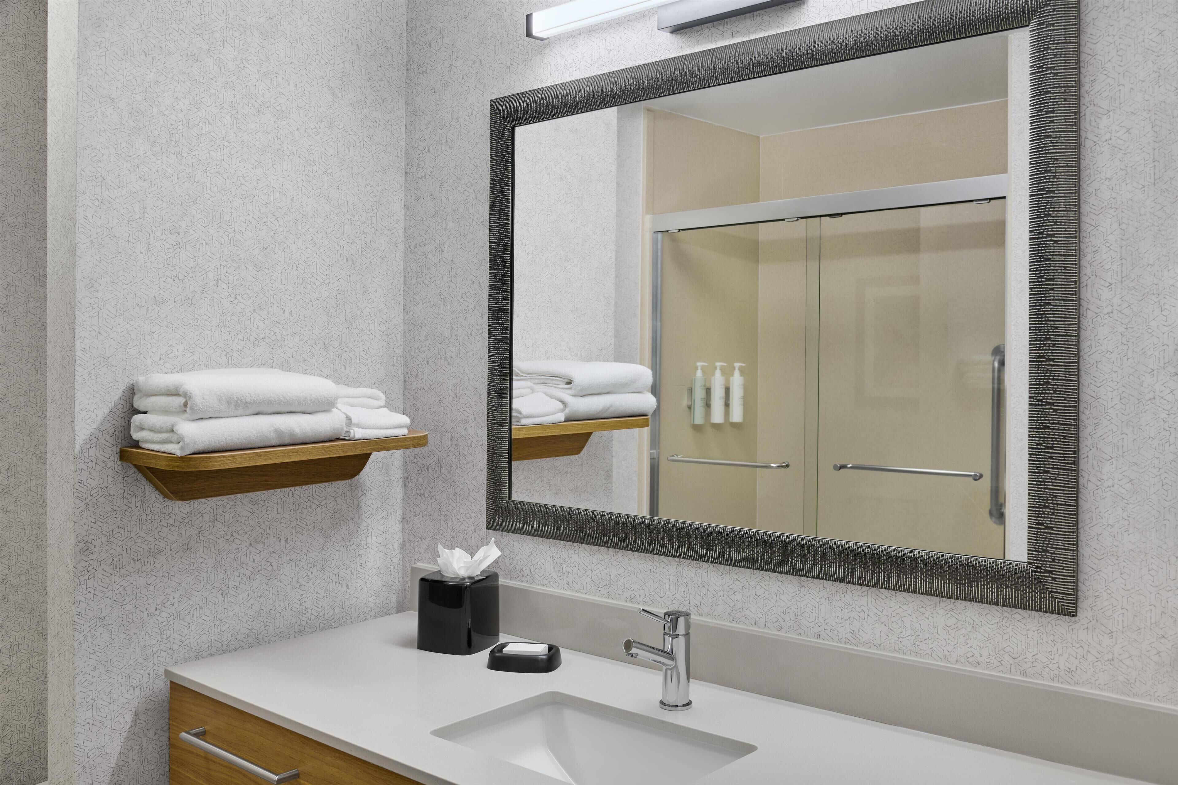 A modern bathroom with a white sink, a large mirror, and a towel rack.