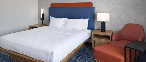A hotel room with a bed, a nightstand, a chair, and a table.