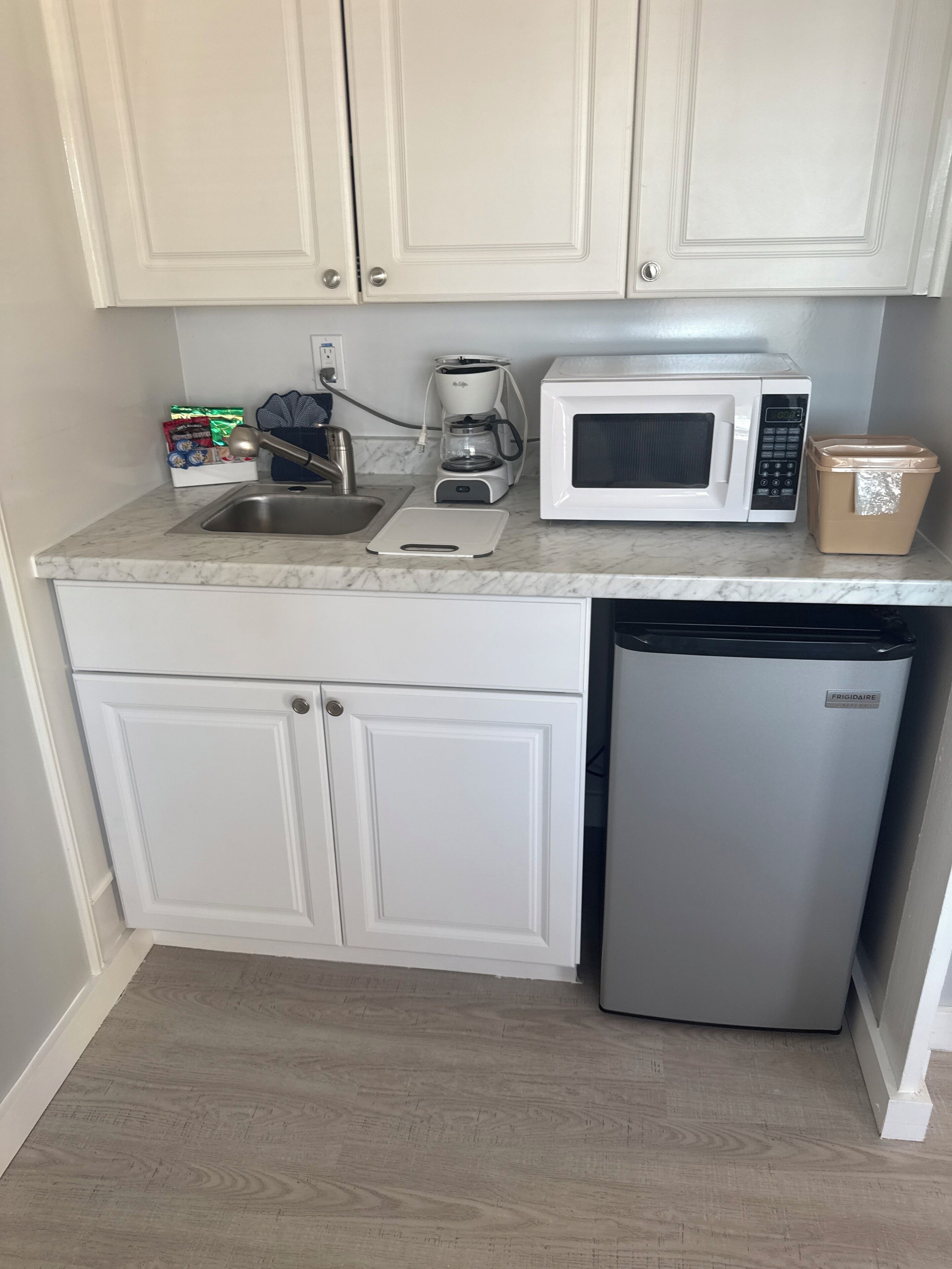 A compact kitchen with white cabinets, a stainless steel sink, a coffee maker, a microwave, and a refrigerator.