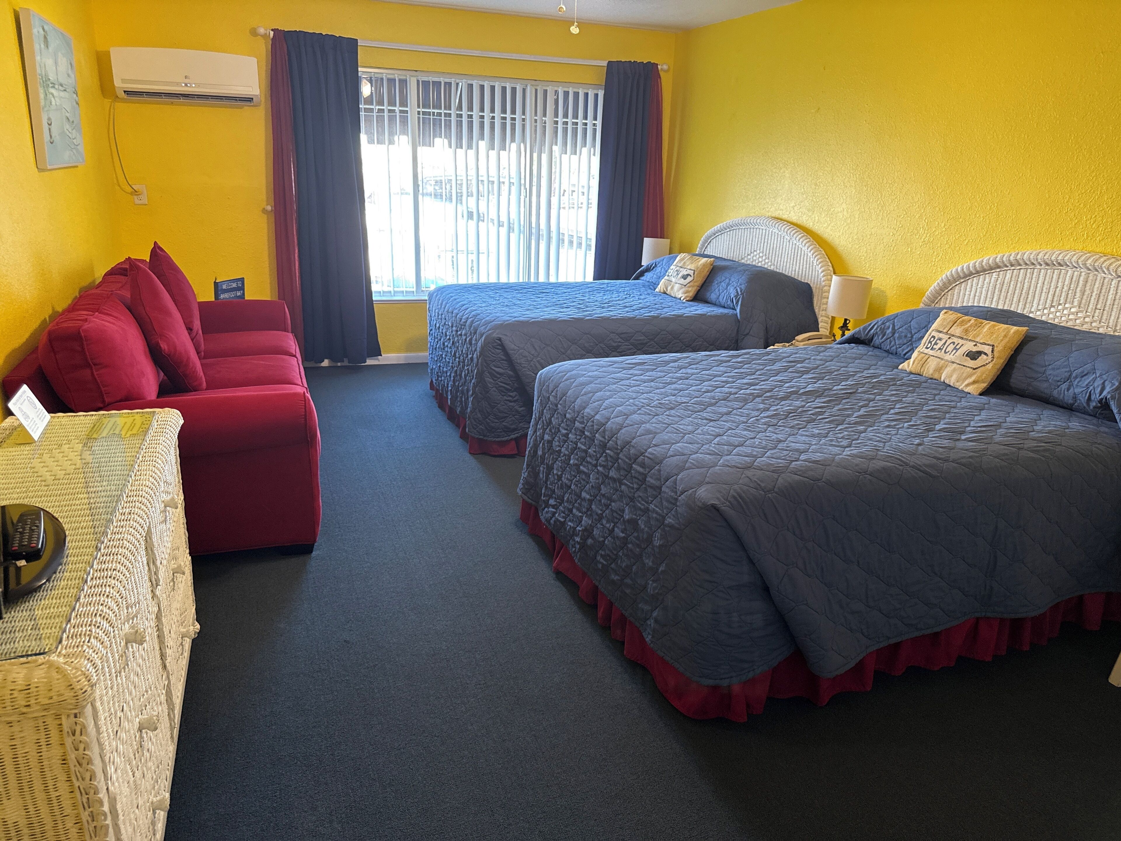 A hotel room with two beds, a red sofa, and a wicker chair.