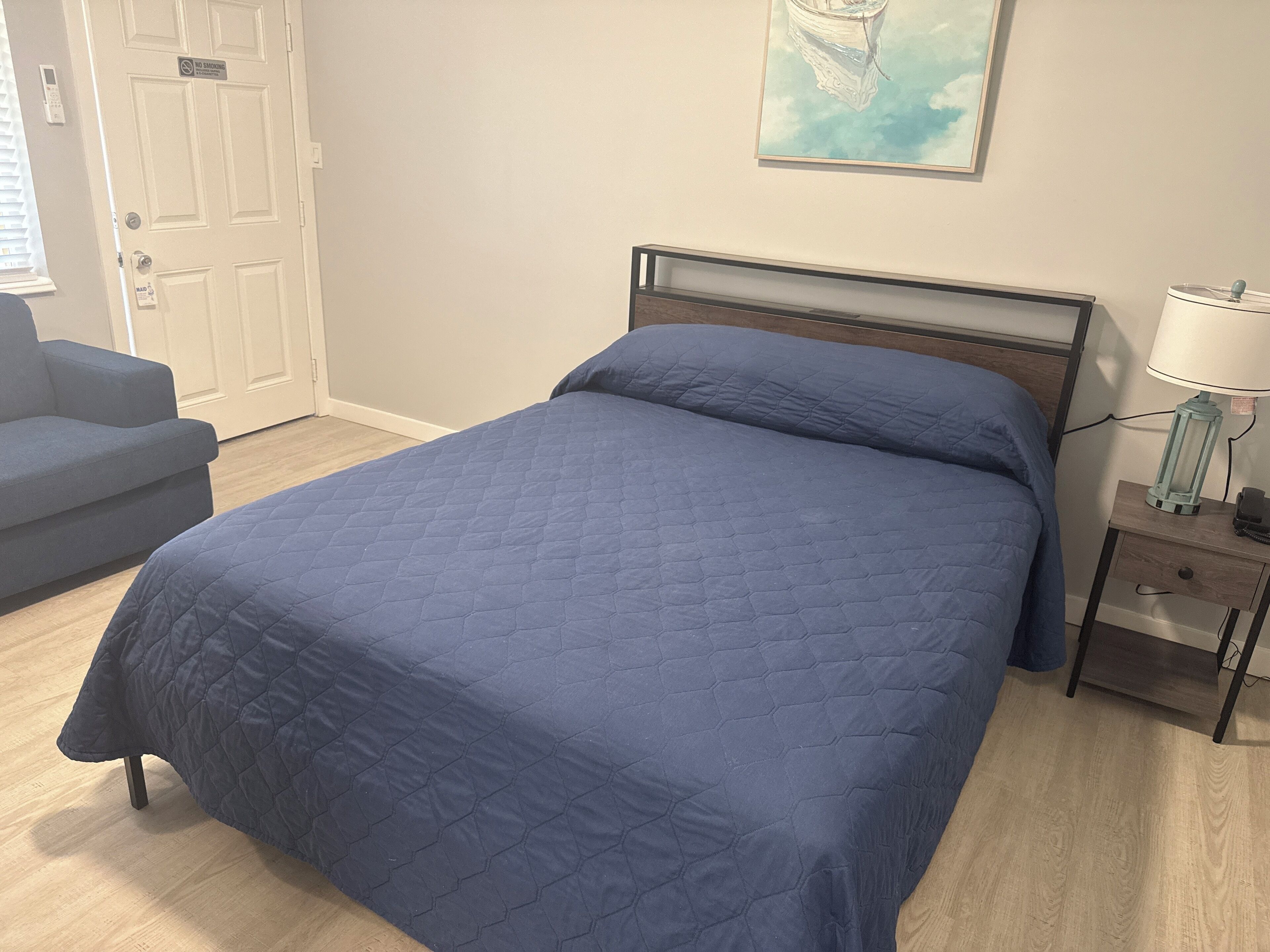 A bedroom with a bed, a nightstand, a lamp, a chair, and a door.