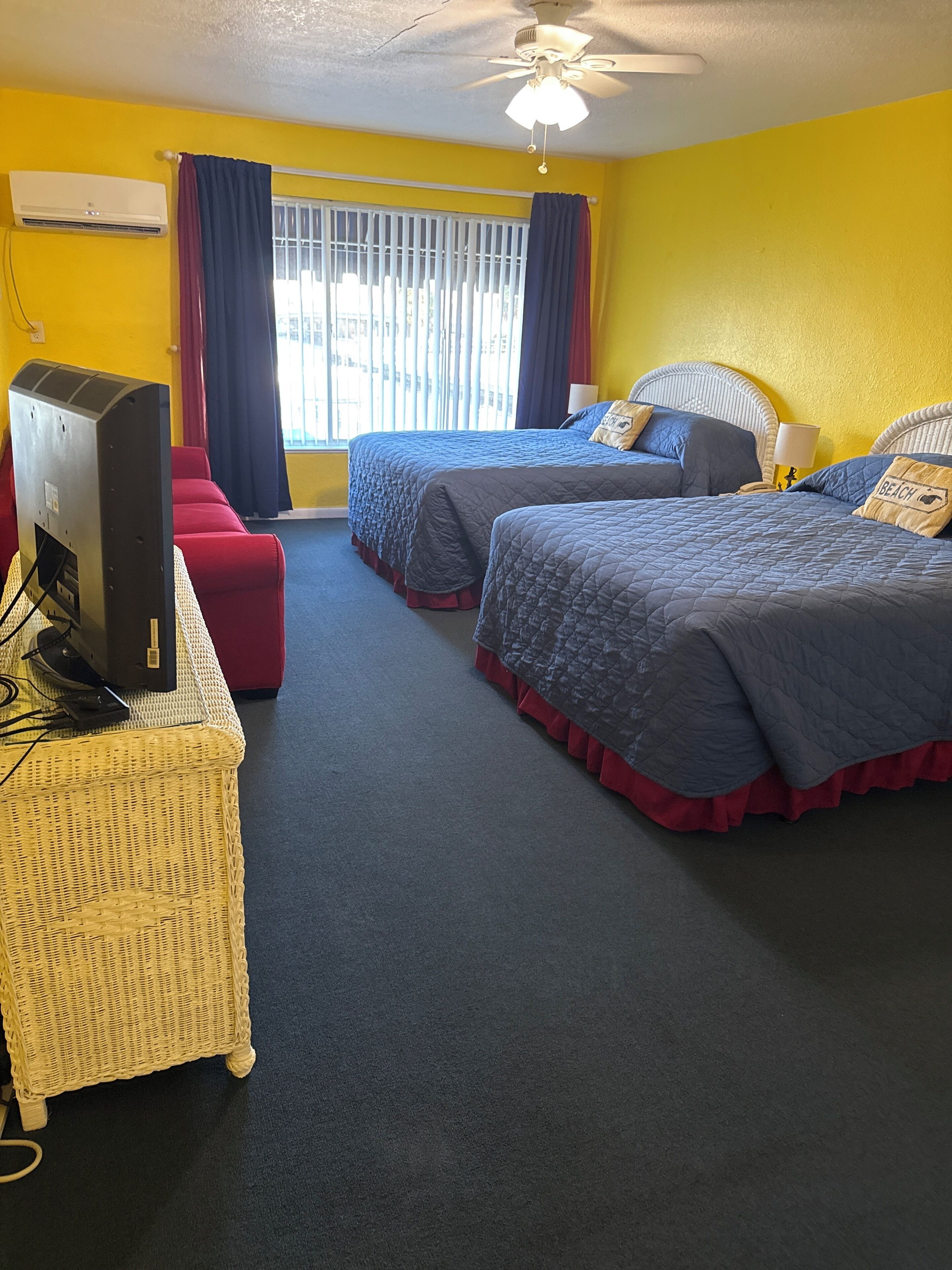 A hotel room with two beds, a television, a desk, and a window with curtains.