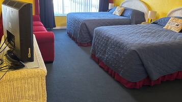 A hotel room with two beds, a television, a desk, and a window with curtains.