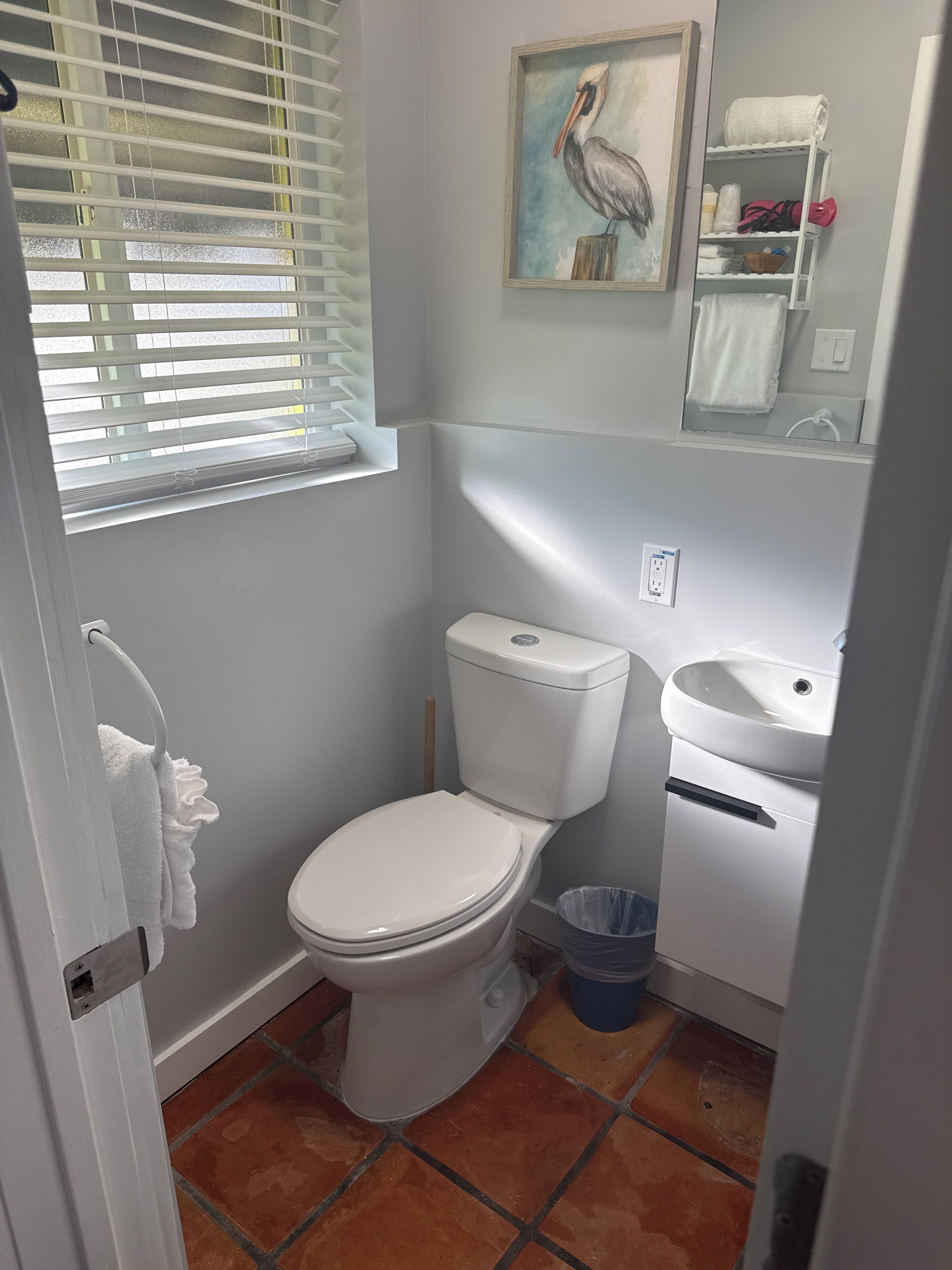 Un baño pequeño y limpio con inodoro, lavamanos y ventana con persianas.