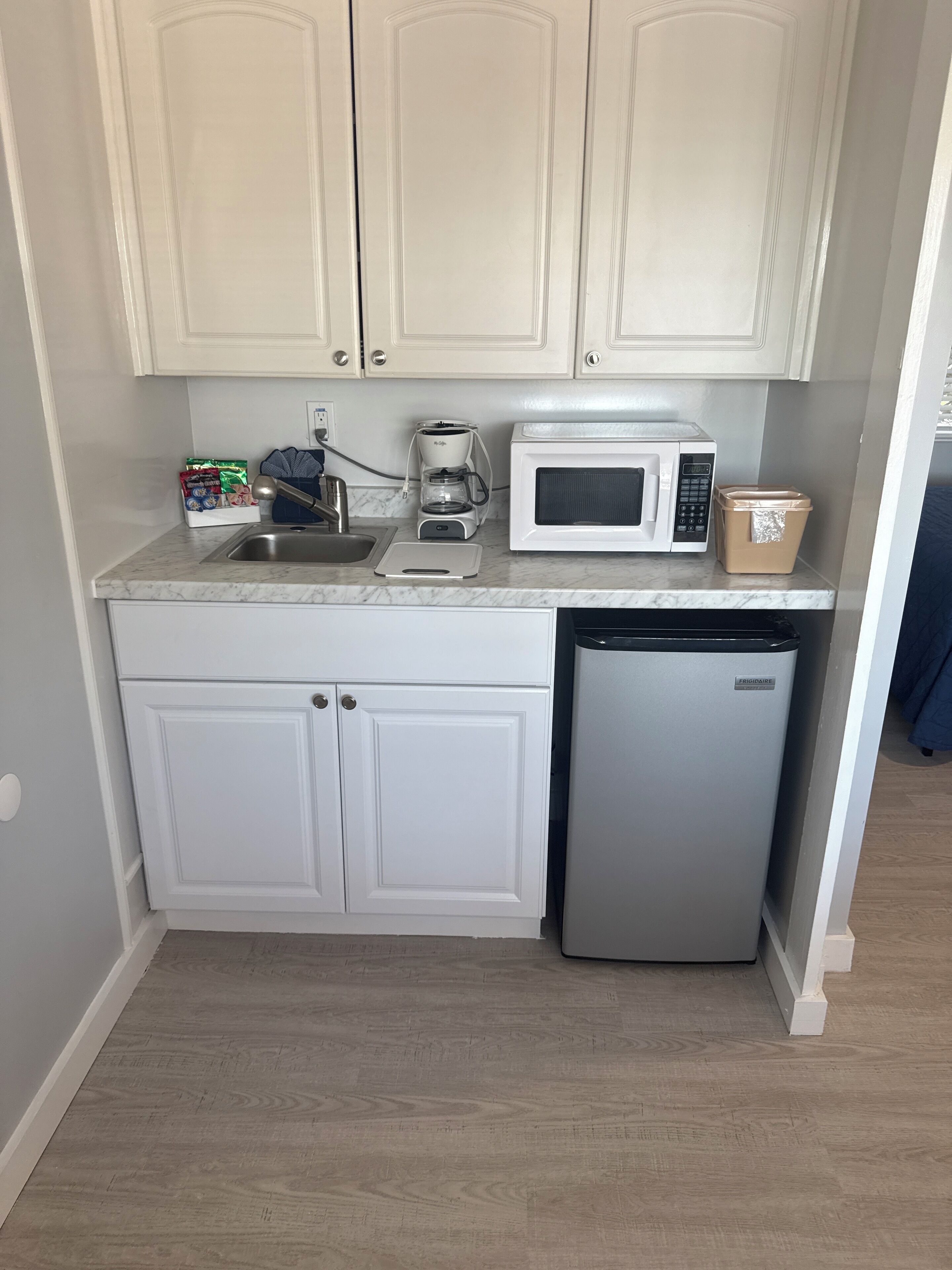 Eine kleine Küche mit weißen Schränken, einer eingebauten Mikrowelle, einer Kaffeemaschine und einem Kühlschrank.
