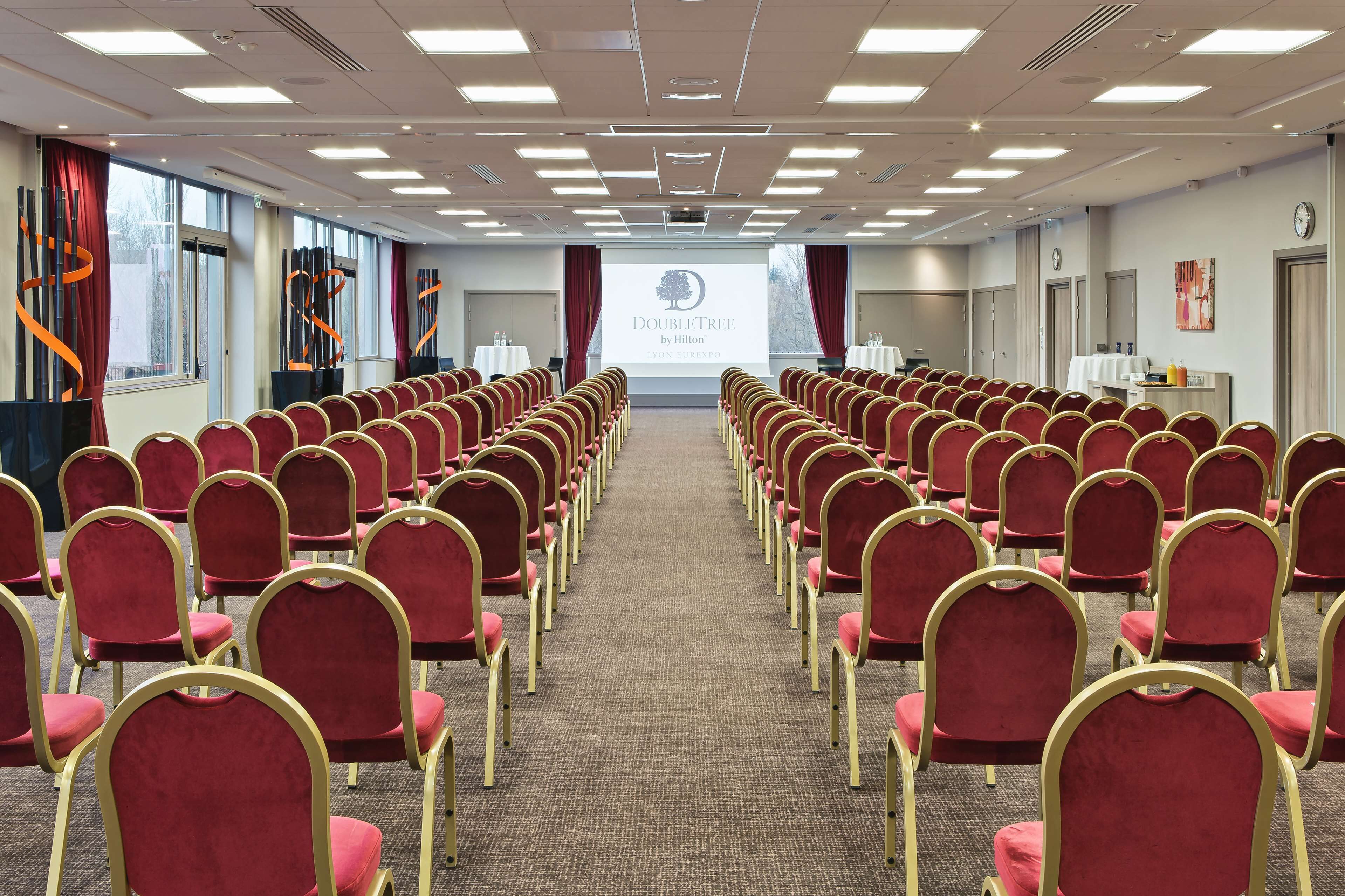 Ett konferensrum med rader av röda stolar, ett heltäckningsmatta och en projektorduk som visar texten ”DOUBLETREE by Hilton”.