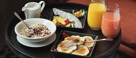 Una bandeja de desayuno con cereal, tortitas, fruta y dos vasos de zumo de naranja.