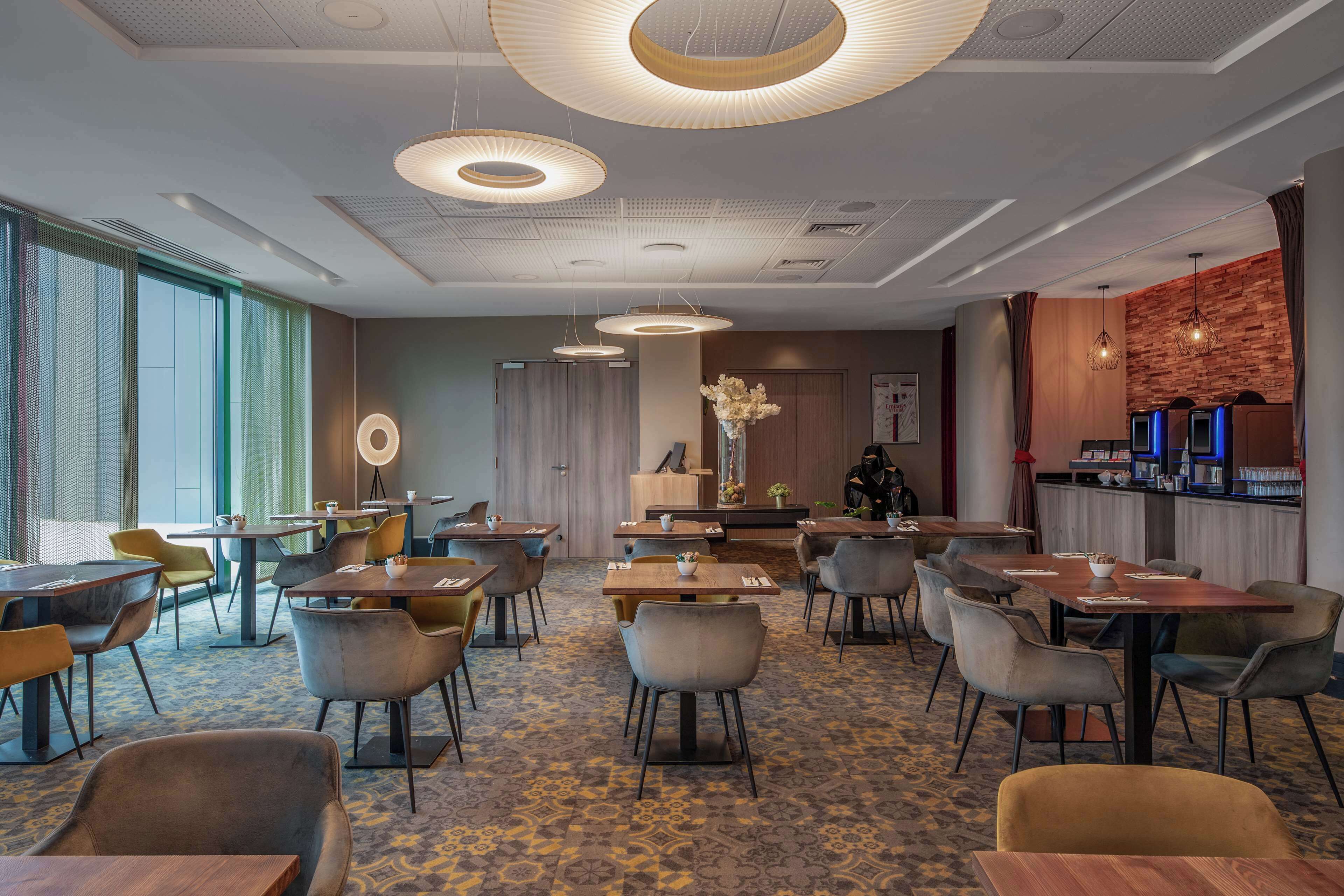 Un espace repas moderne avec des tables et des chaises rondes, un bar éclairé de lumières bleues et une grande fenêtre laissant entrer la lumière naturelle.