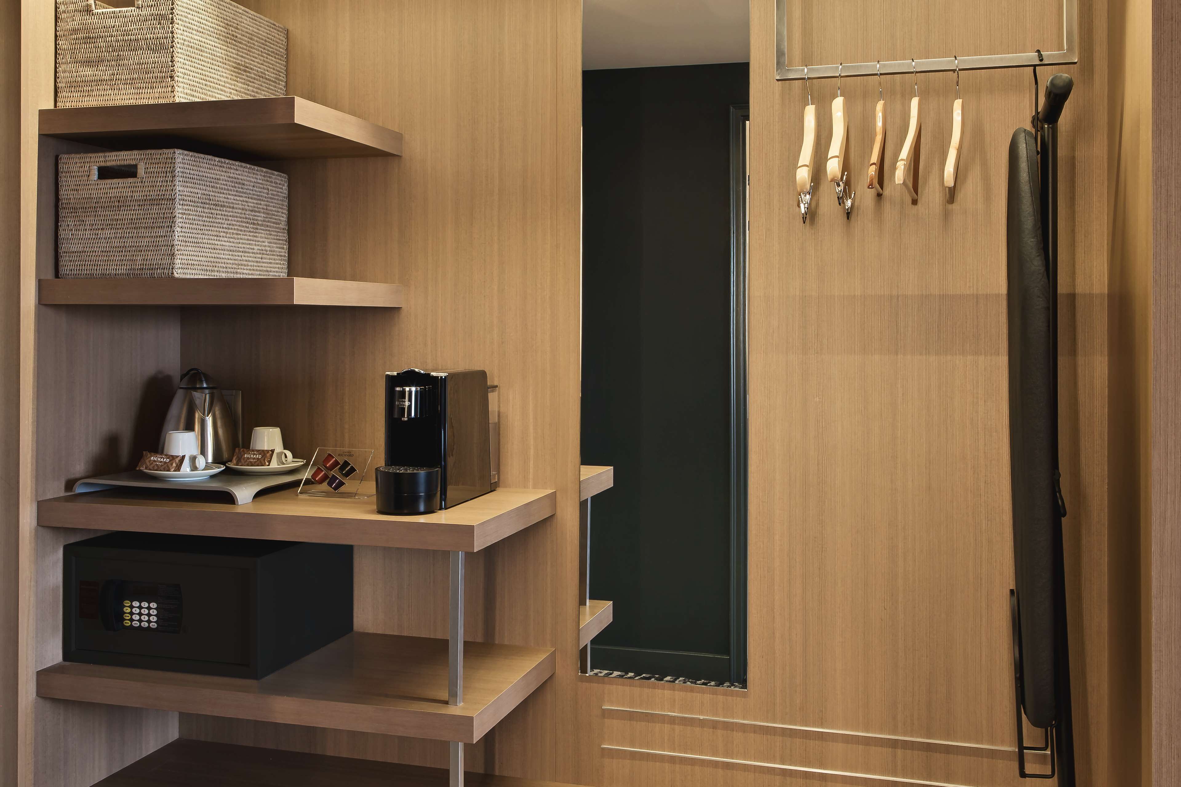 Una habitación de hotel moderna con estanterías de madera, una cafetera y artículos de aseo ordenados.