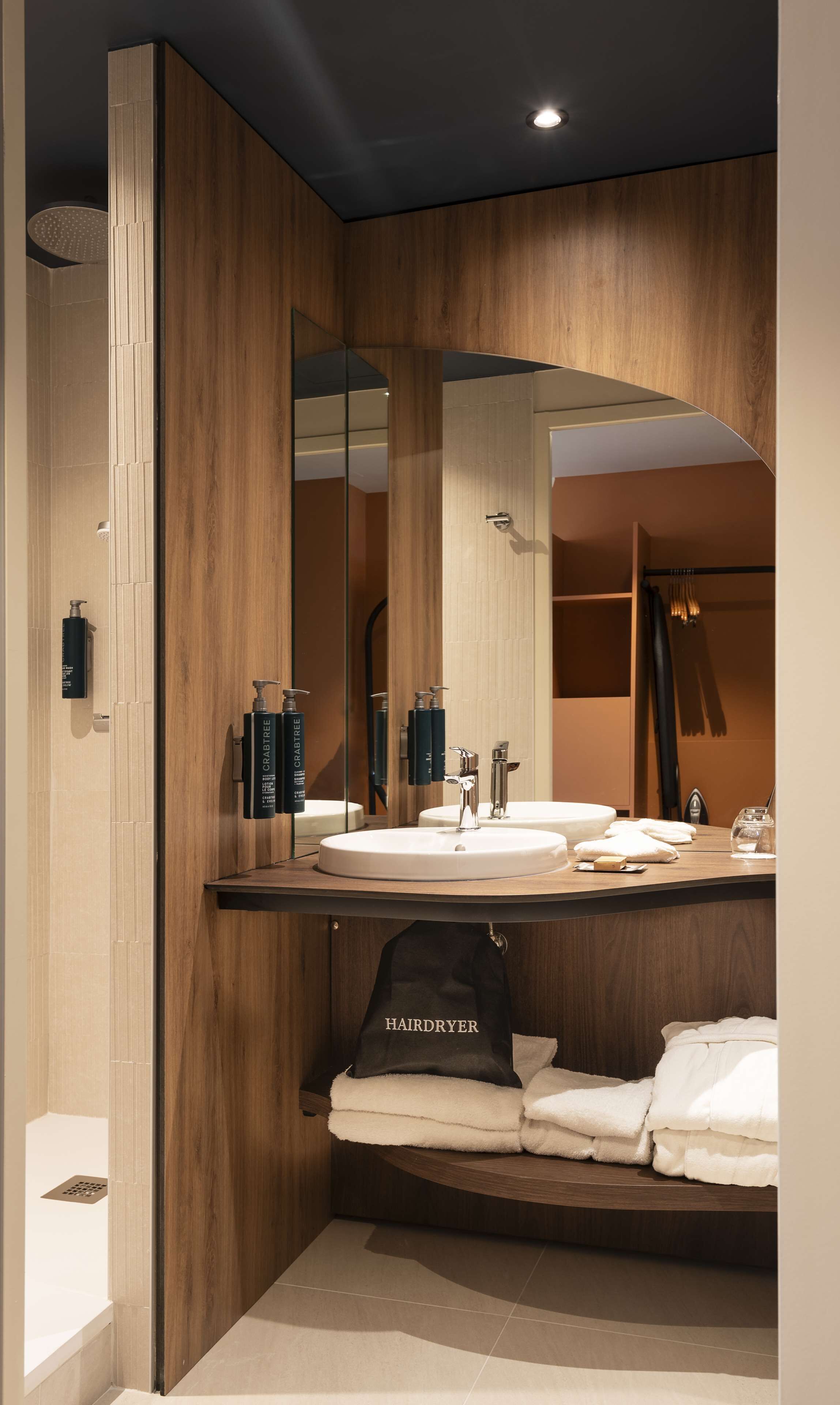 Une salle de bain moderne avec un meuble-lavabo en bois, un grand miroir et un sac pour sèche-cheveux.