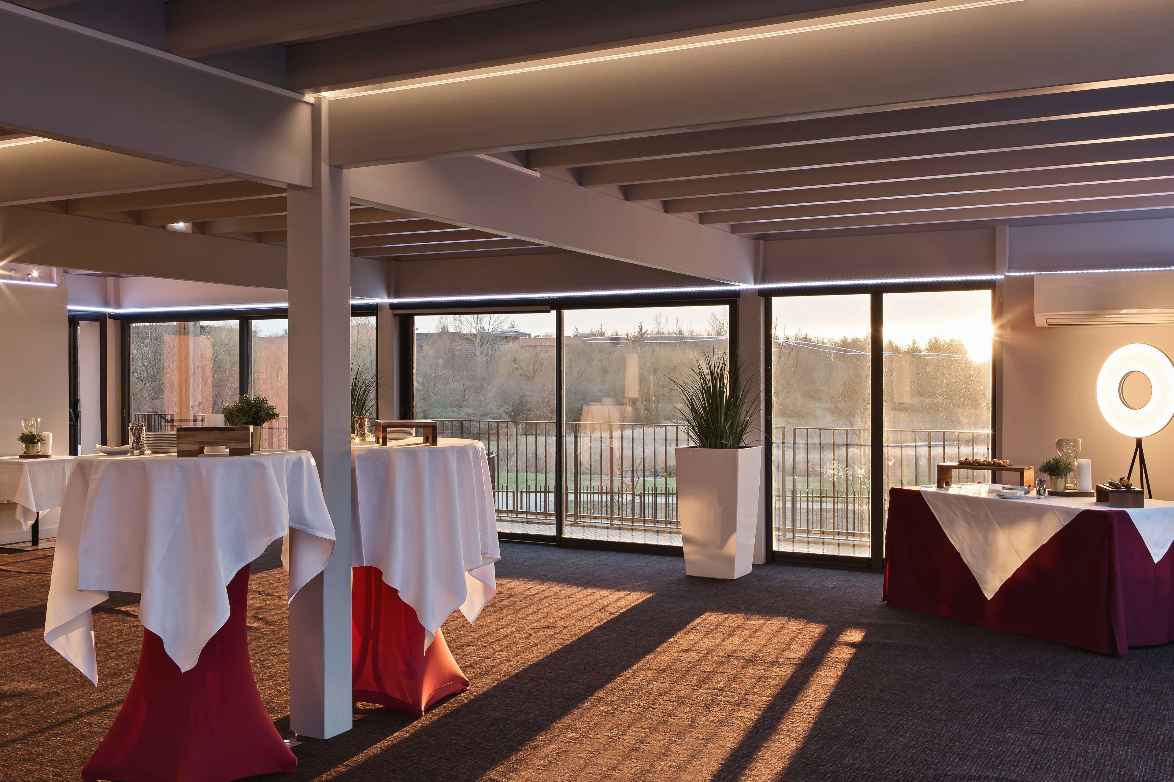A spacious indoor area with tables set up for dining, large windows offering views of the outdoors, and a balcony with a railing.