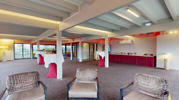 Un salón de conferencias con techos altos, ventanas amplias y una mesa roja con mantel blanco.