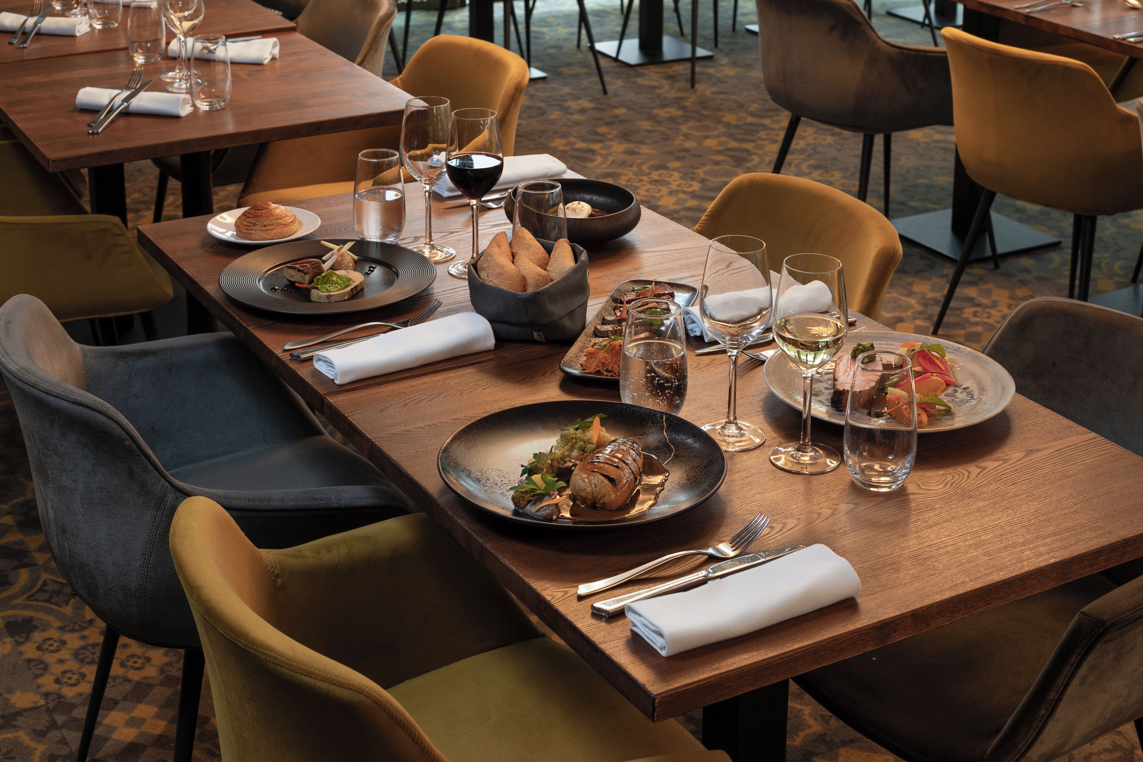 A restaurant setting with a long table set for dining, including plates of food, glasses, and cutlery.