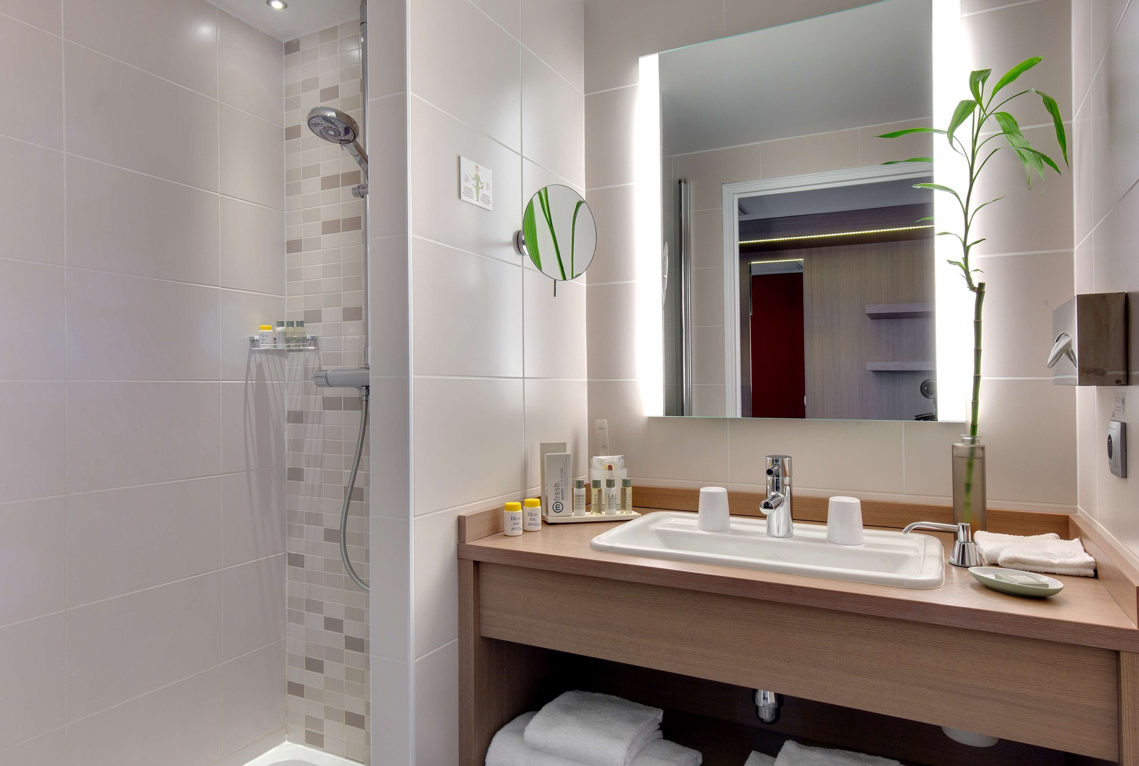 A modern bathroom with a shower, a sink with a mirror, and a potted plant.