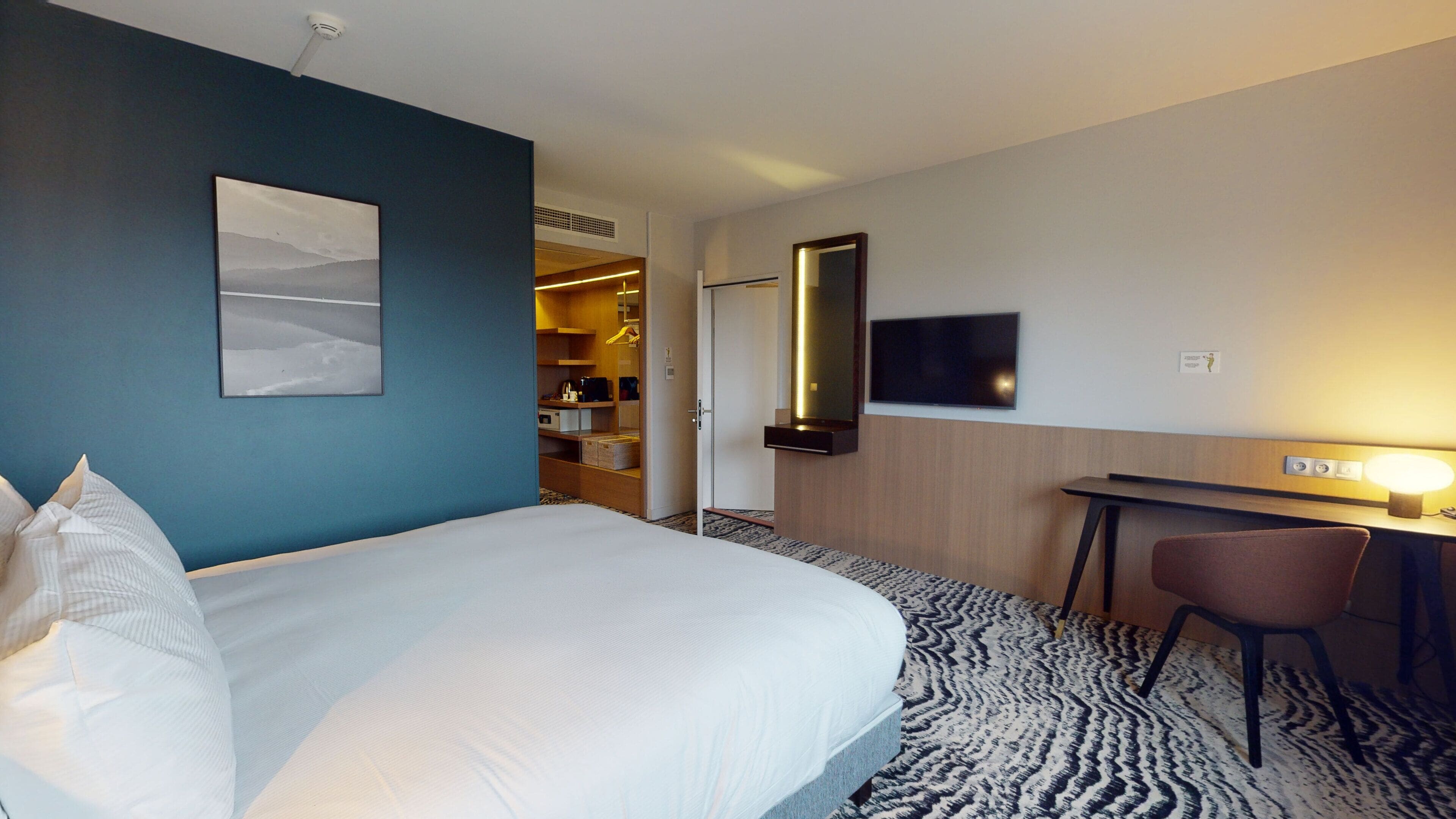 A hotel room with a bed, a desk, a chair, a TV, and a wardrobe.