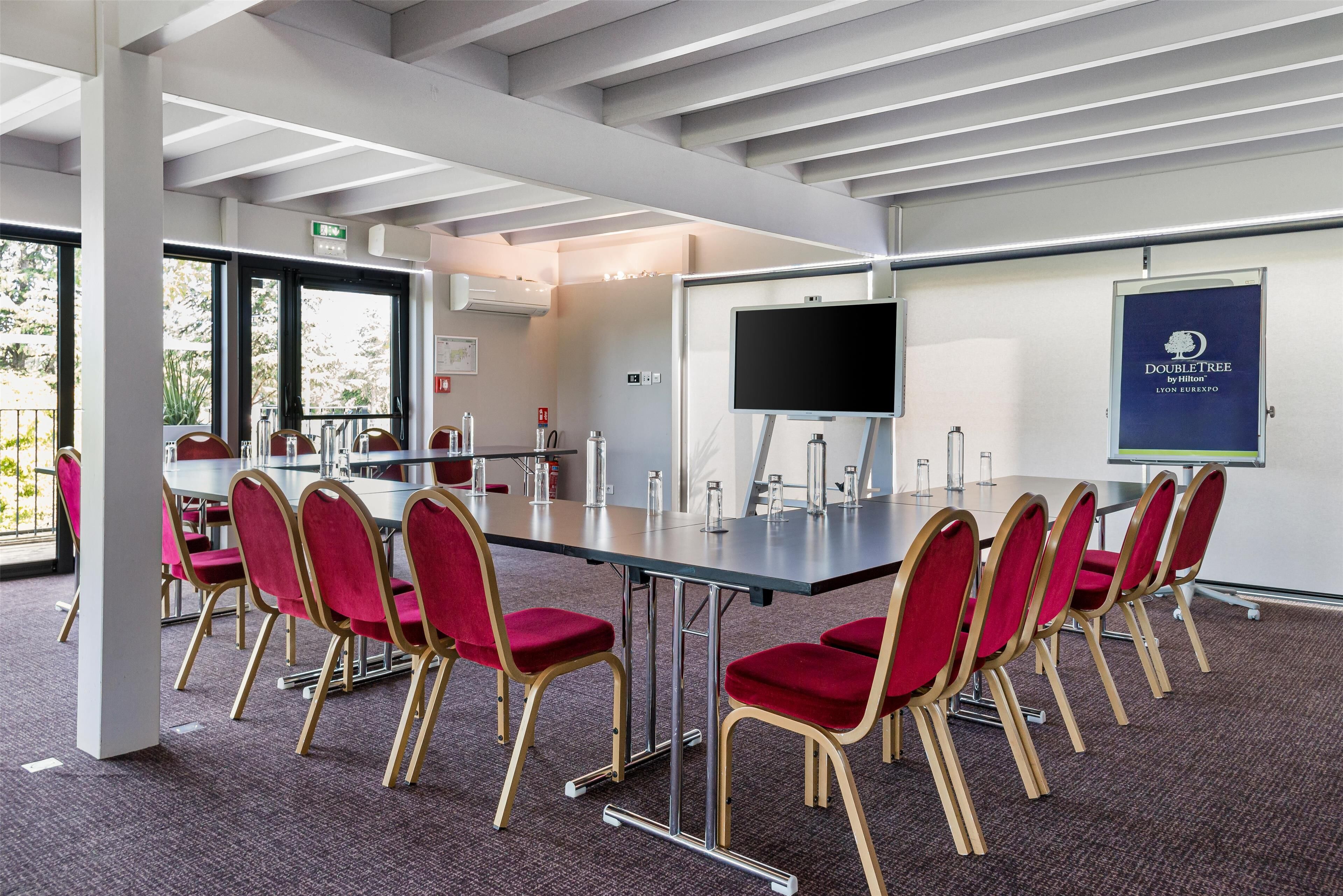 A conference room with a long table, red chairs, a whiteboard, and a screen.