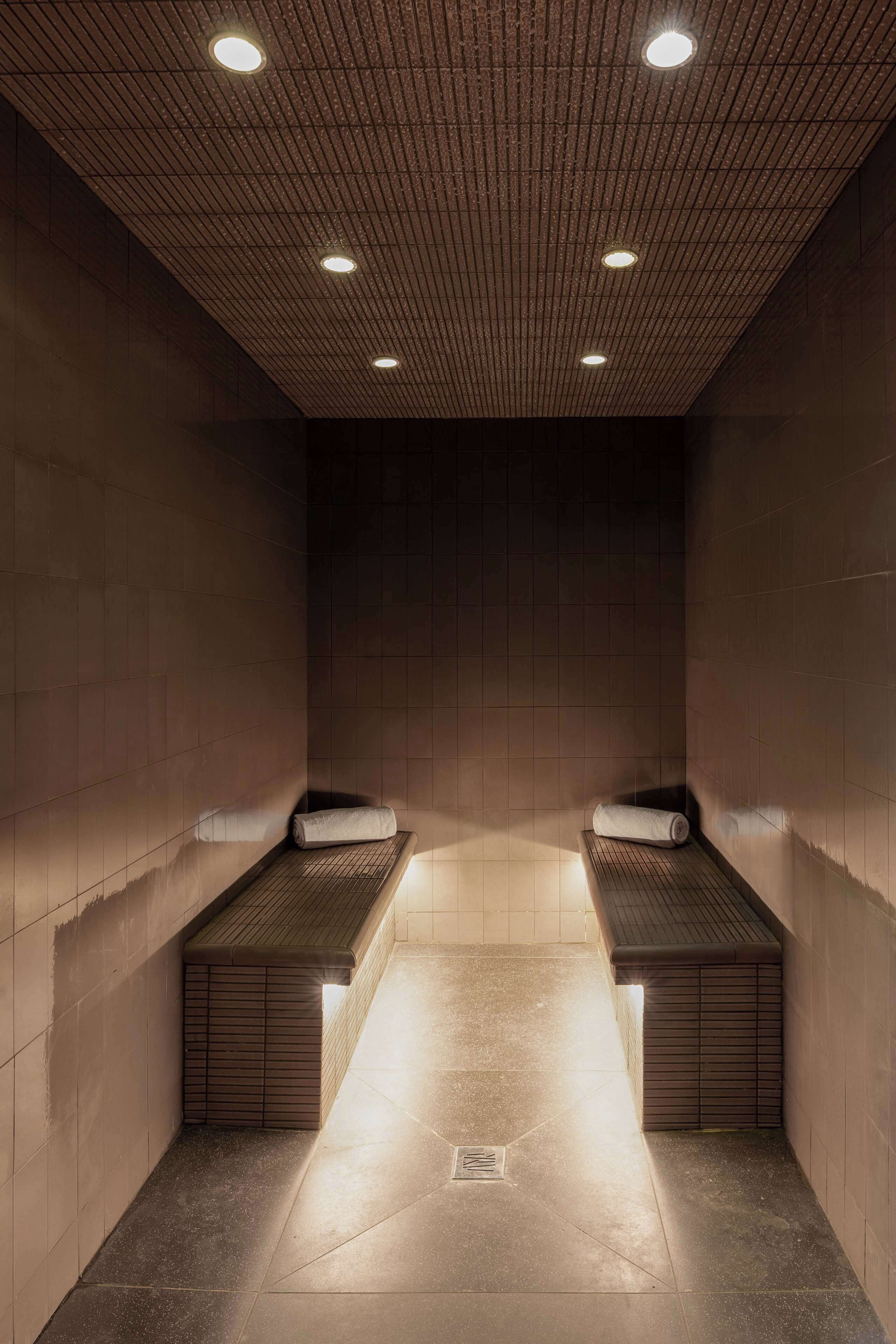 Un sauna con dos bancos, suelo de baldosas e iluminación empotrada en el techo.